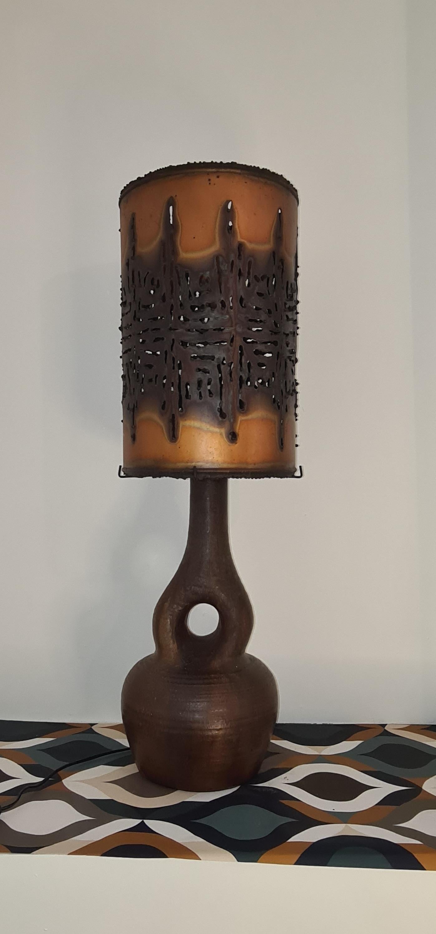 magnifique lampe en céramique Accolay, toute l'originalité de la lampe réside dans l'imposant abat-jour en cuivre perforé qui diffuse une lumière douce.
L'abat-jour repose sur un socle composé de 4 tiges de fer, l'une de ces tiges est légèrement