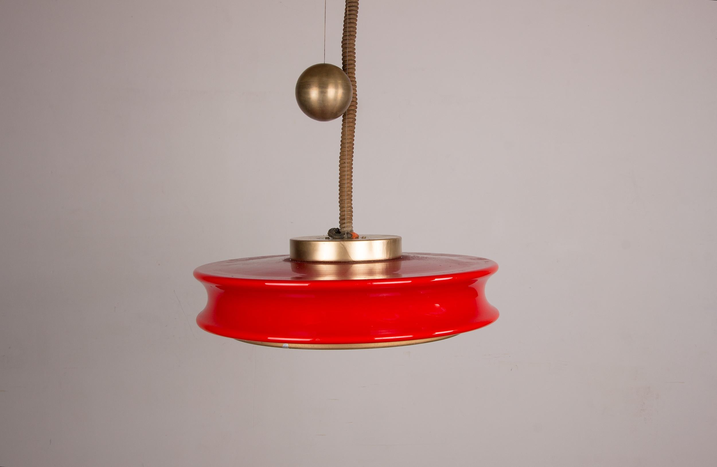Exceptional large pendant chandelier, with a heavy spherical brass counterweight that allows height adjustment, a magnificent large red glass diffuser in a circular, contoured shape, and a gold grille with a concentric pattern at the base.
It
