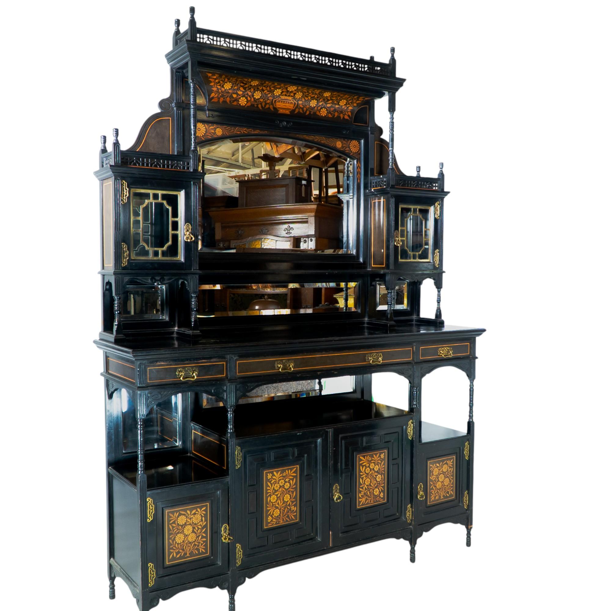 Attributed to Henry William Batley, probably for Gillows of Lancaster. A large Aesthetic Movement ebonized walnut cabinet with fine finials and a fretwork gallery to the top, and an arched canopy below with vibrant inlaid floral decoration and a