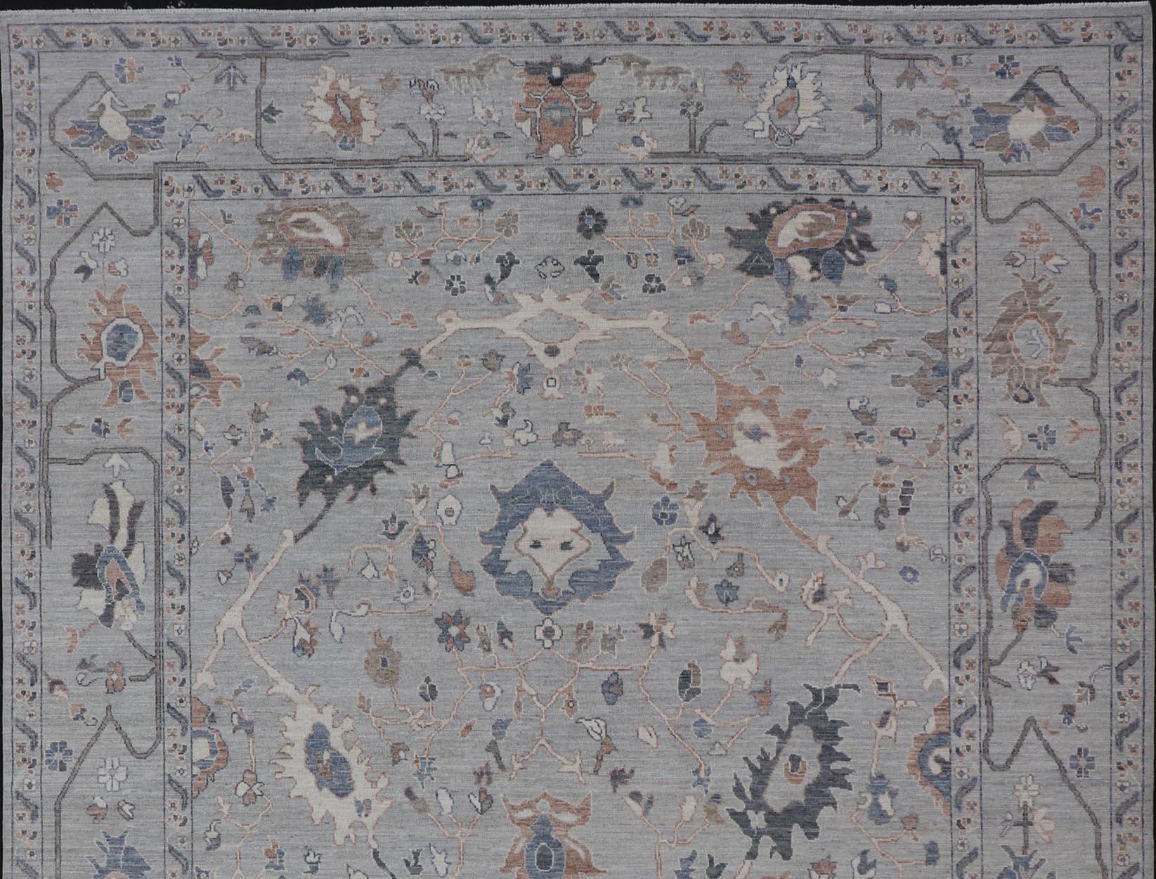 This hand-knotted Oushak has a very classic feel with a slight twist. This rug only has one background color, reaching from border to field in a muted gray tone. The distinct angular floral design from this region is shown in light brown, denim