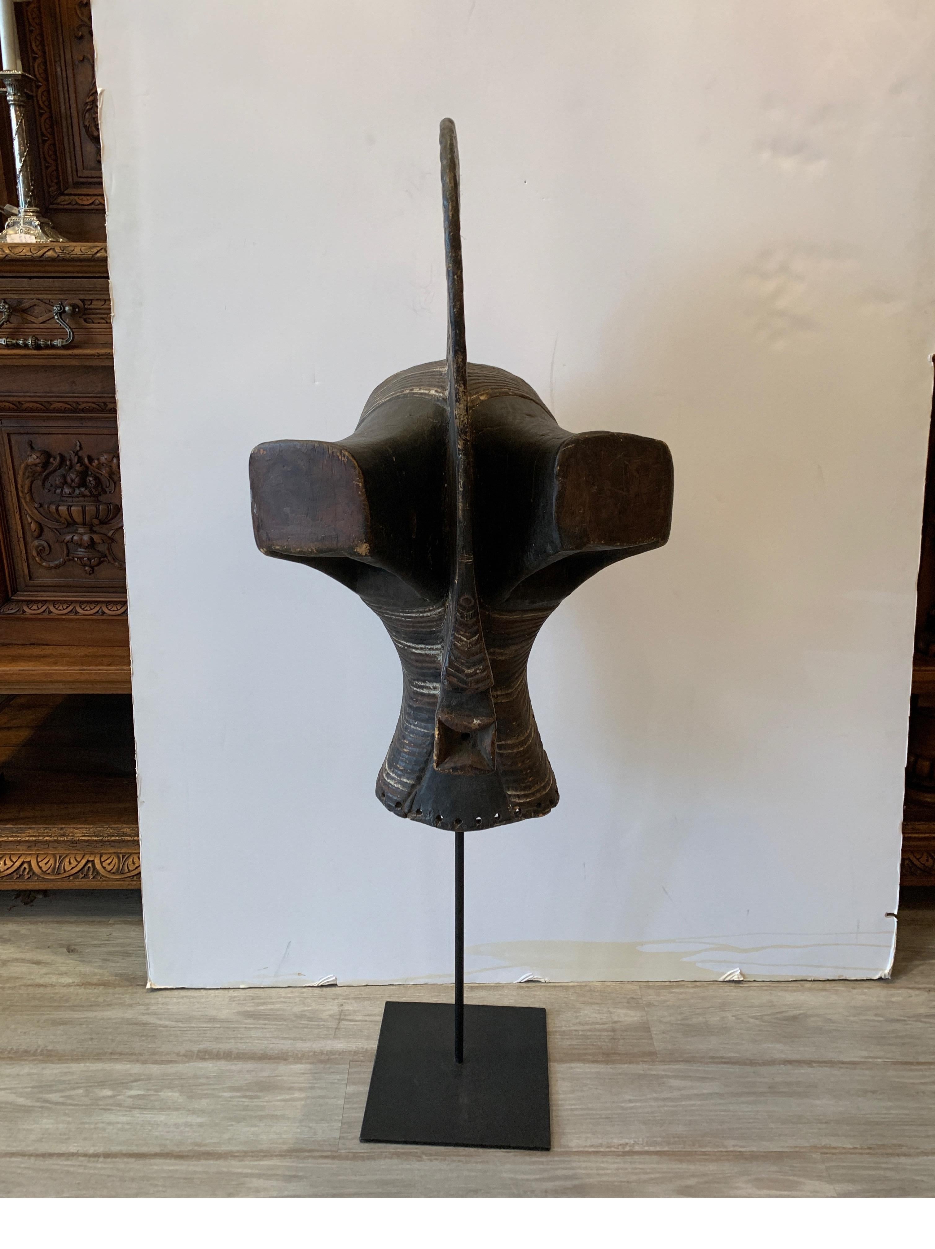 Very stylish hand carved African mask on a custom stand. The front with very textured surface with painted details, there is some shrinkage and separation at the seams due to age. The black metal base made for proper display.