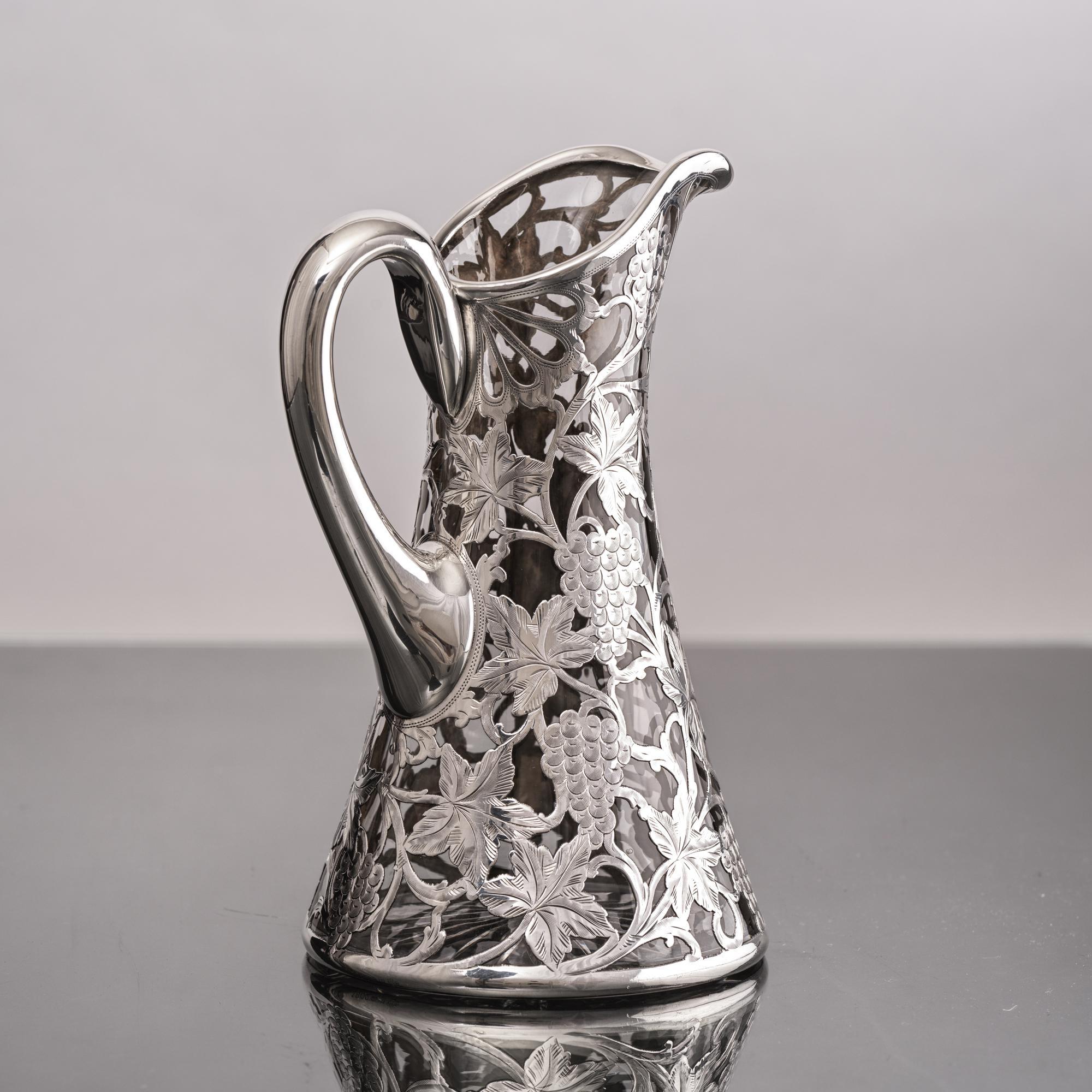 Antiker Wasser- oder Weinkrug mit einem elegant geformten Glaskörper, überzogen mit 999er Silber in einem durchbrochenen Design mit Trauben, Weinblättern und Ranken, alles handgraviert.  In den Glasboden ist ein klares Starburst-Muster