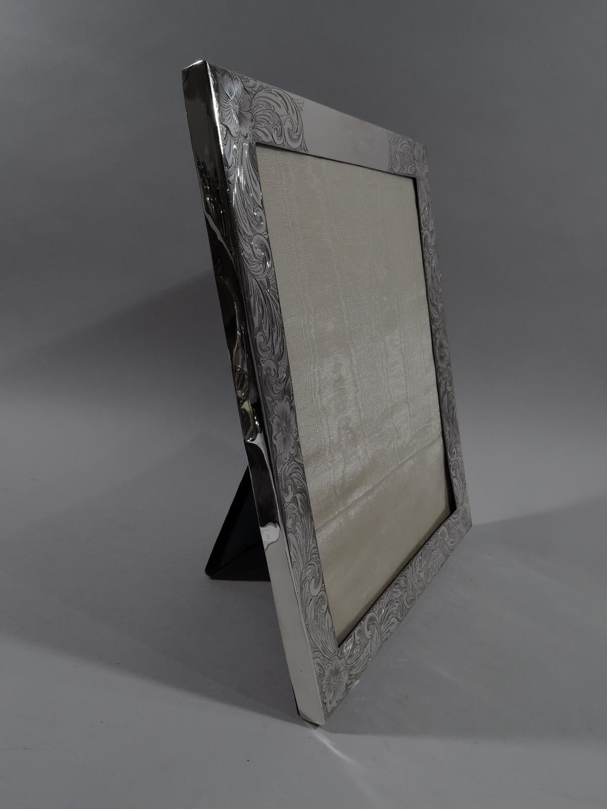 Large American Art Nouveau sterling silver picture frame. Rectangular window in flat surround engraved dense and dynamic scrolls and flowers; sides plain. Top rail has shaped cartouche (vacant). With glass, silk lining, and velvet back and hinged