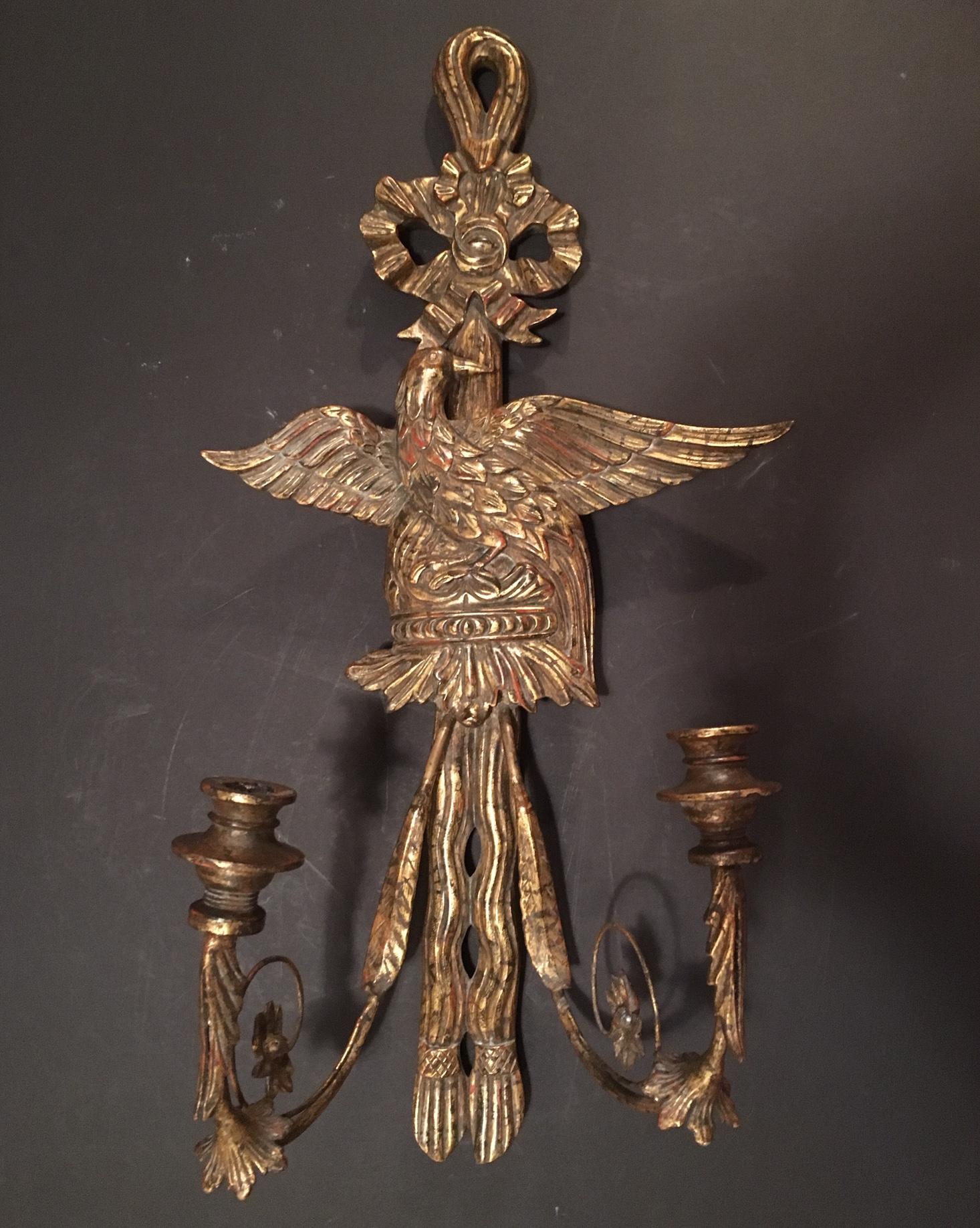 This wood carved and gold gilded antique sconce features a majestic eagle with spread wings beneath a tied bow. The candle arms are of patinated scrolled brass and very finely detailed with acanthus leaves and carved wooden drip pans. The red base