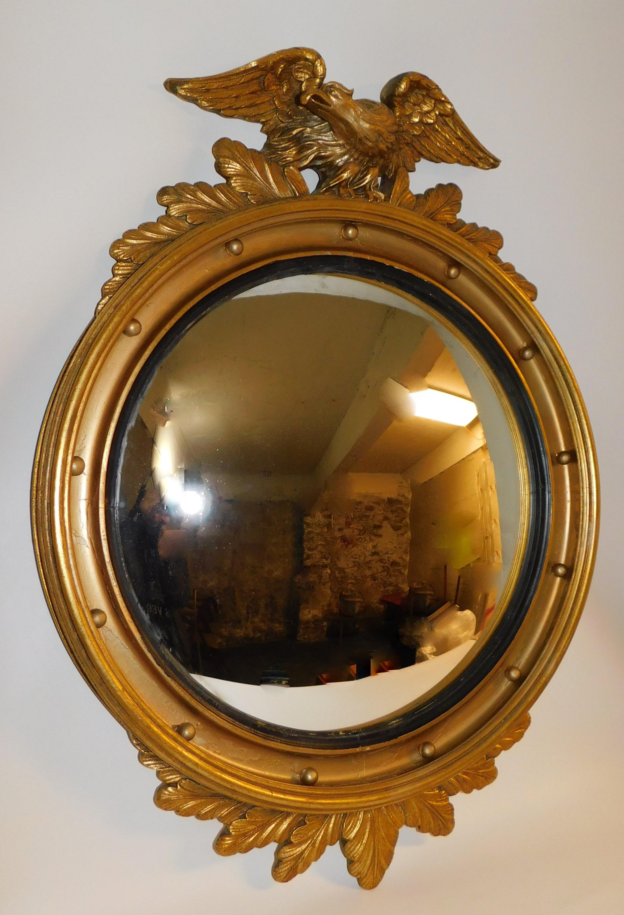Large antique 19th century American gilt carved wood oval convex mirror with eagle perched to flee on top, circular interior spheres, and fitted ebonized reeded ring covered in gilding that is mostly intact. Mirror retains the original glass, tape
