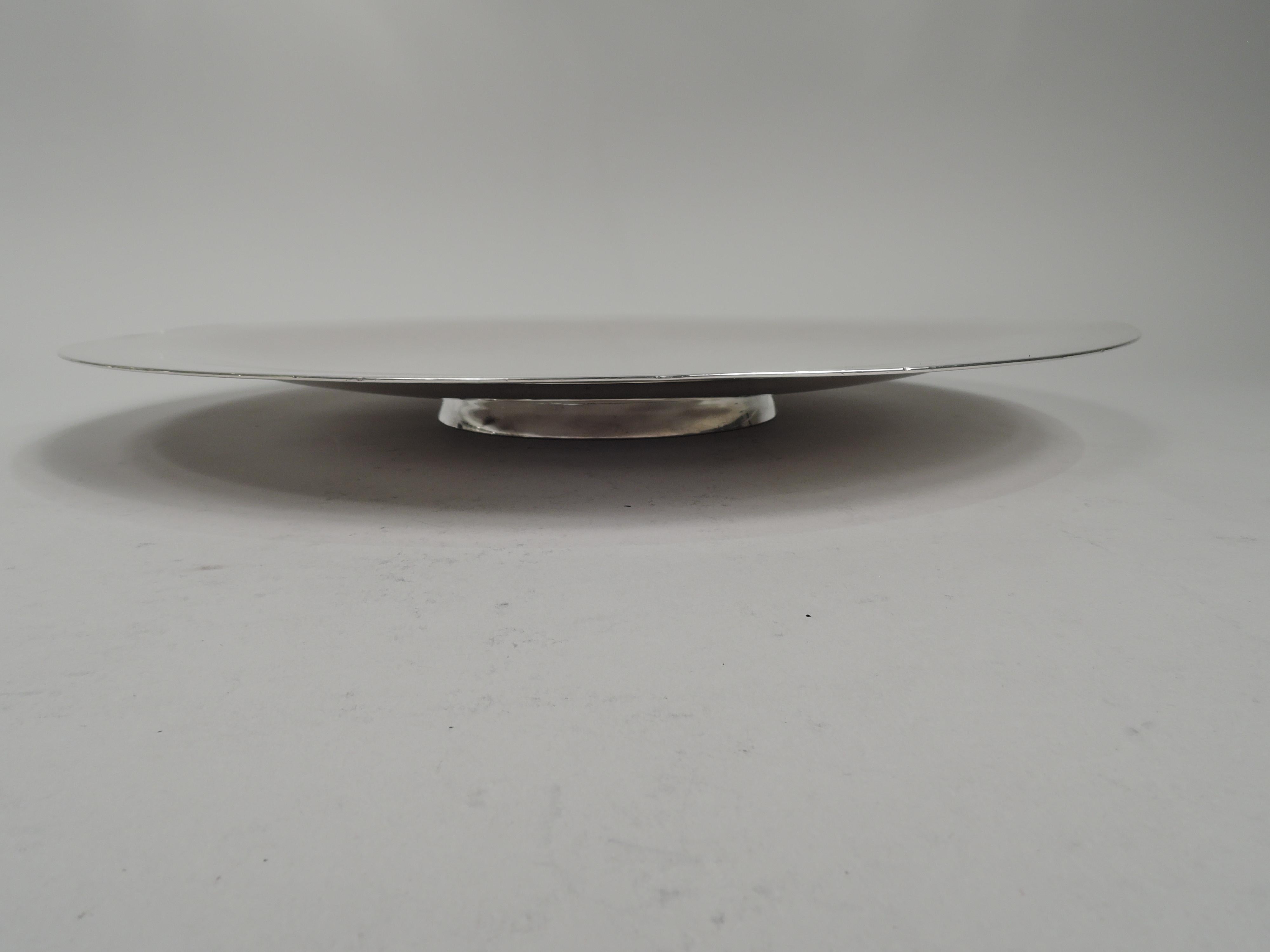 Mid-Century Modern sterling silver serving plate. Made by International Silver Co. in Meriden, Conn. Round with shallow integral well. Short and spread foot. Stark and functional. Fully marked including maker’s stamp and no. AH6269L. Heavy weight:
