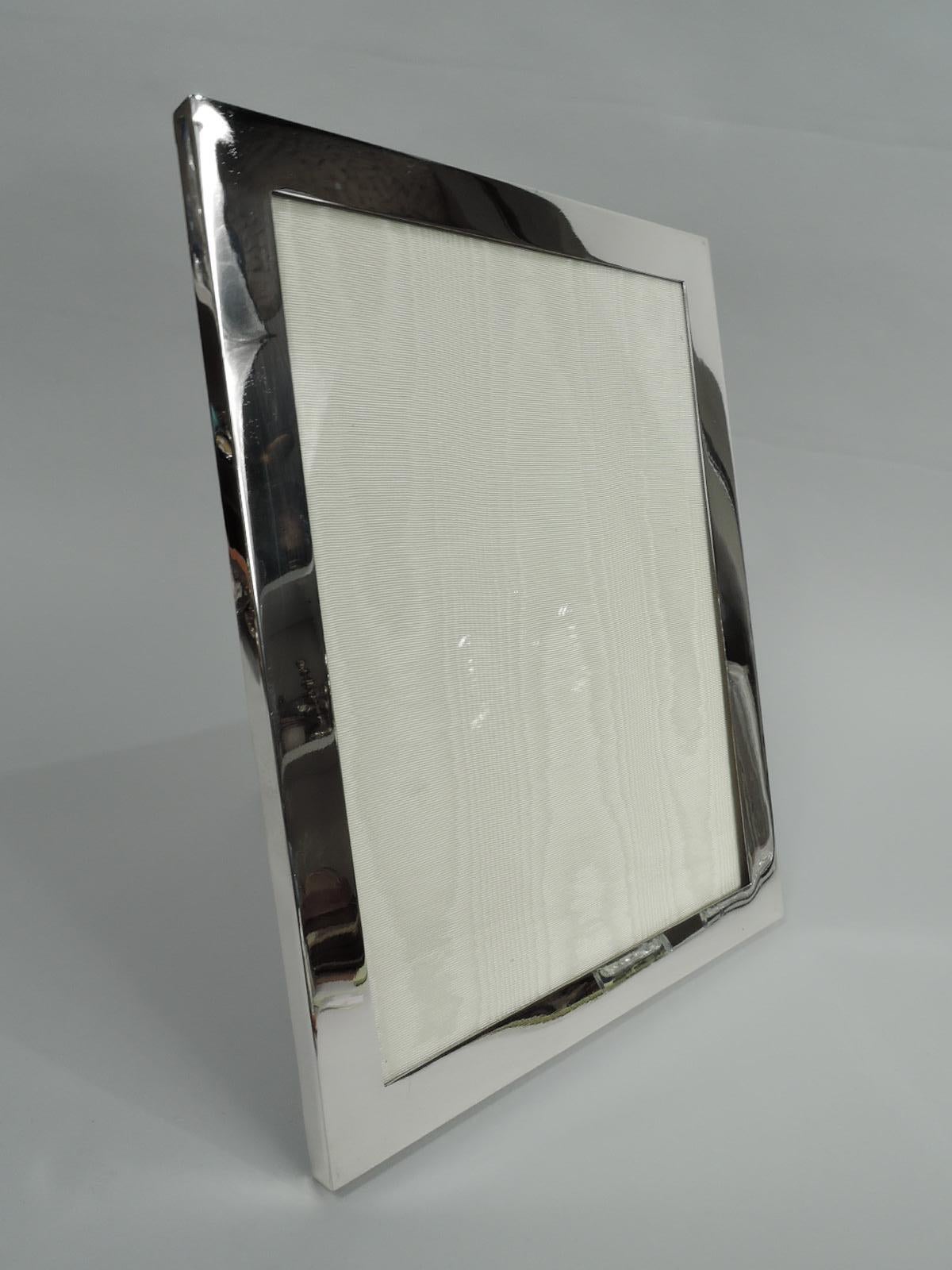 Mid-Century Modern sterling silver picture frame. Made by International Silver Co. in Meriden, Conn. Rectangular window in plain flat surround. With glass, silk lining, and laminate back and hinged easel support for portrait (vertical) display.