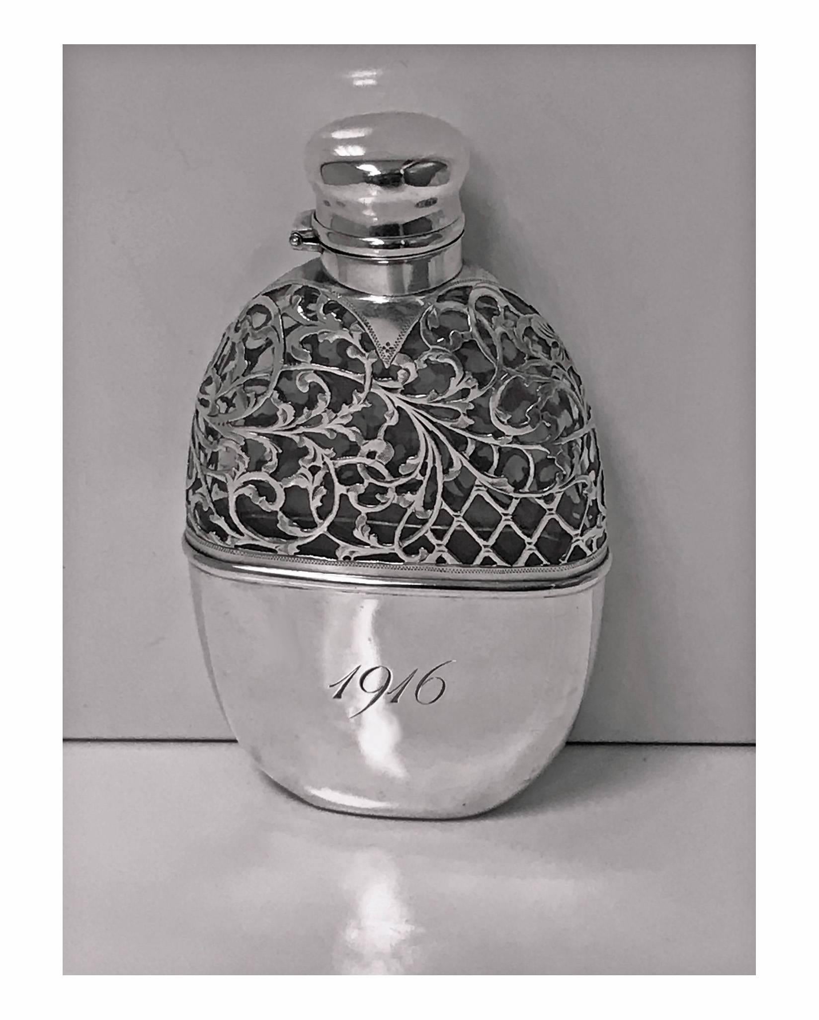 Sterling overlay hip flask, American, circa 1900. The flask with detachable cup, engraved 1916 on one side and intertwining initials, possibly CEH on the other side. The top with thick sterling overlay on clear glass bottle, bayonet hinged cover,