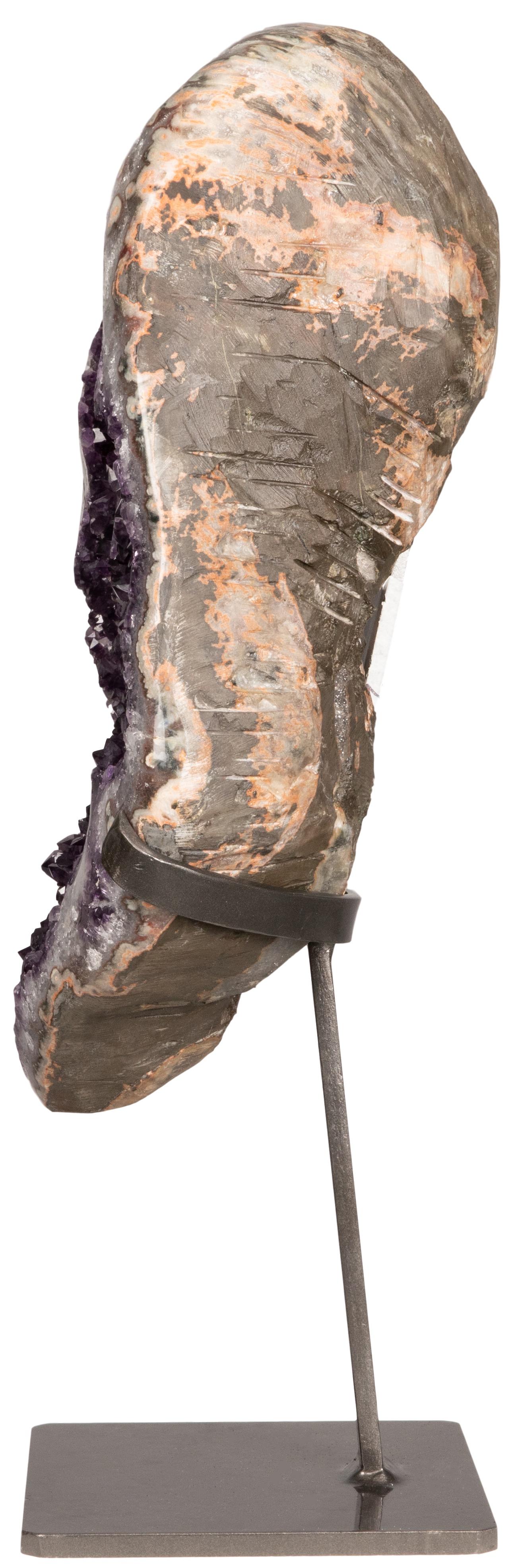 This natural sculpture presents the viewer with deep purple amethyst and a variety of color due to white quartz, green celadonite, and some artful inflections of pink and orange agate. 

The cut and polished stalactites on the interior are