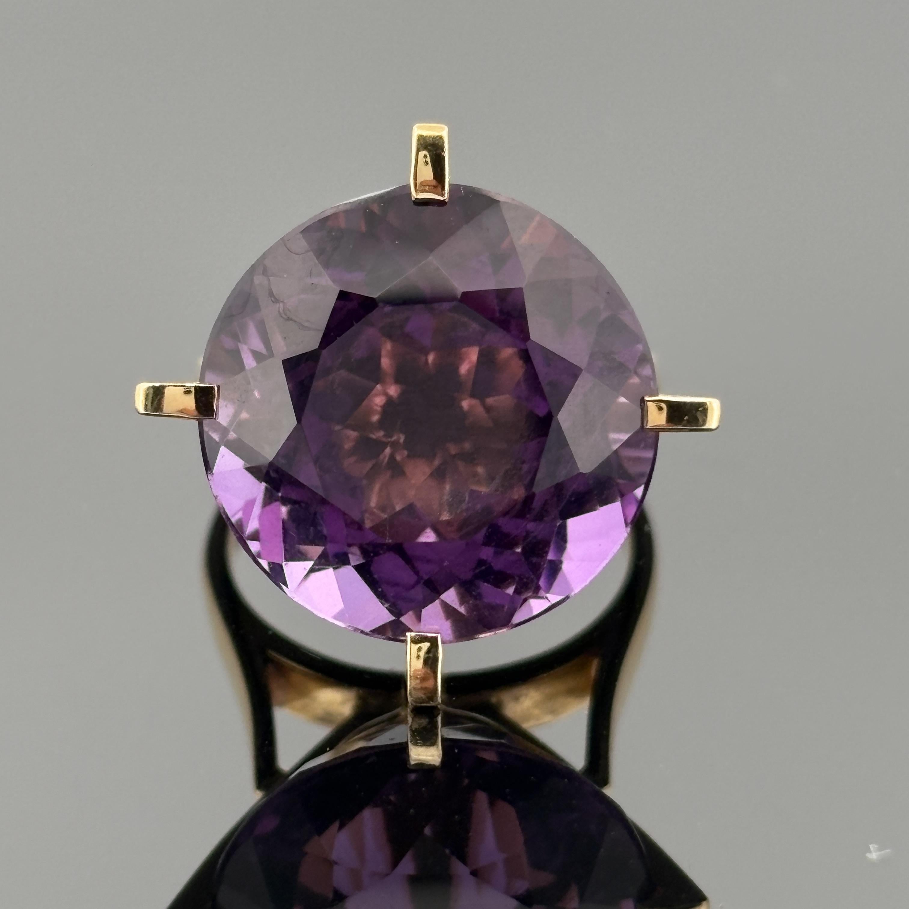 Cette bague de cocktail spectaculaire présente une impressionnante améthyste de taille ronde d'environ 17,01 carats, qui brille d'une teinte violette profonde et vibrante. La pierre précieuse est sertie dans une monture sculpturale en or jaune 18