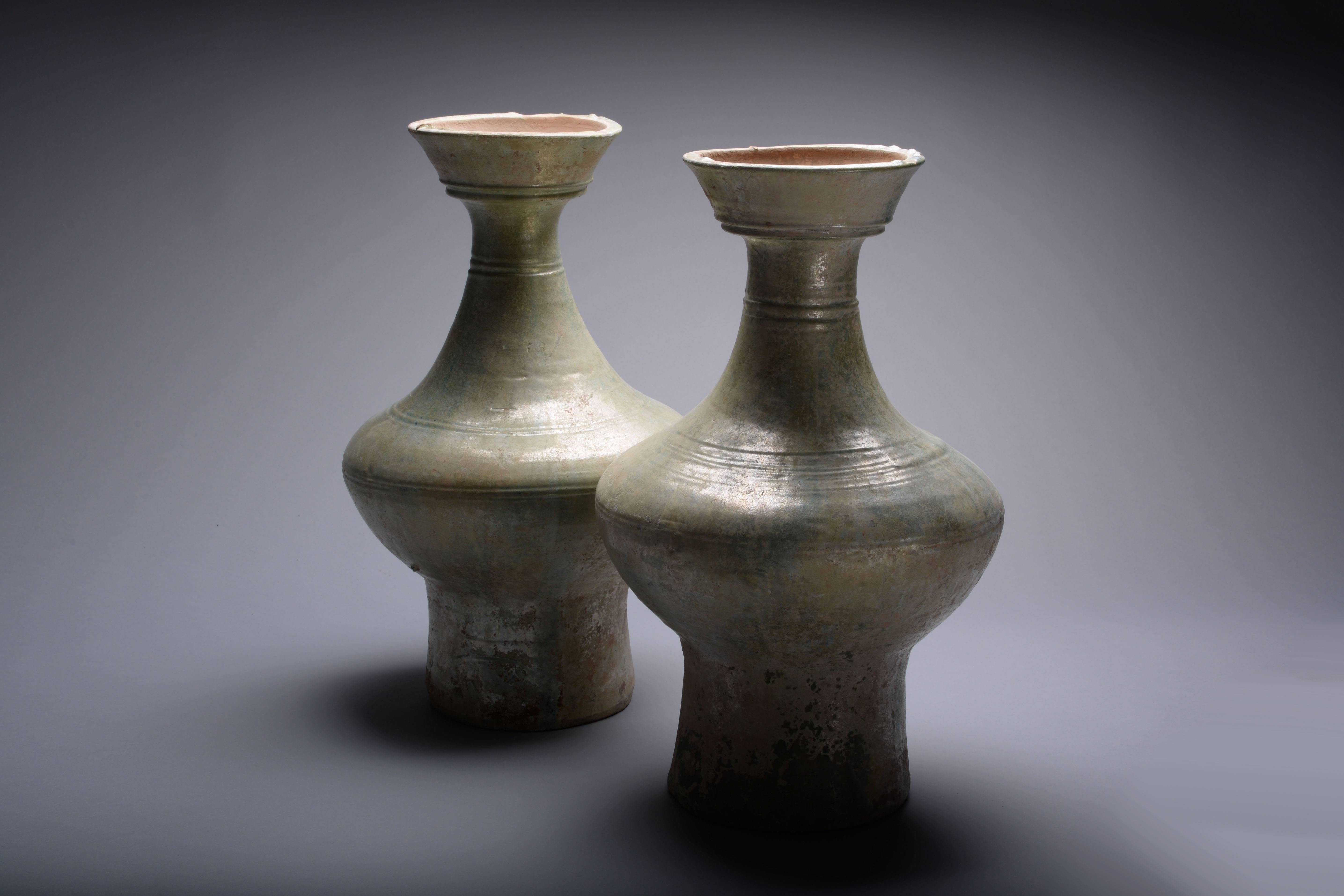 A pair of large ancient Chinese green glazed vases, dating to China's Han dynasty, circa 206 BC-220 AD.

Of undulating, elegant form, the piriform bodies glisten with a silvery green glaze.

These beautiful vases were used as storage vessels for