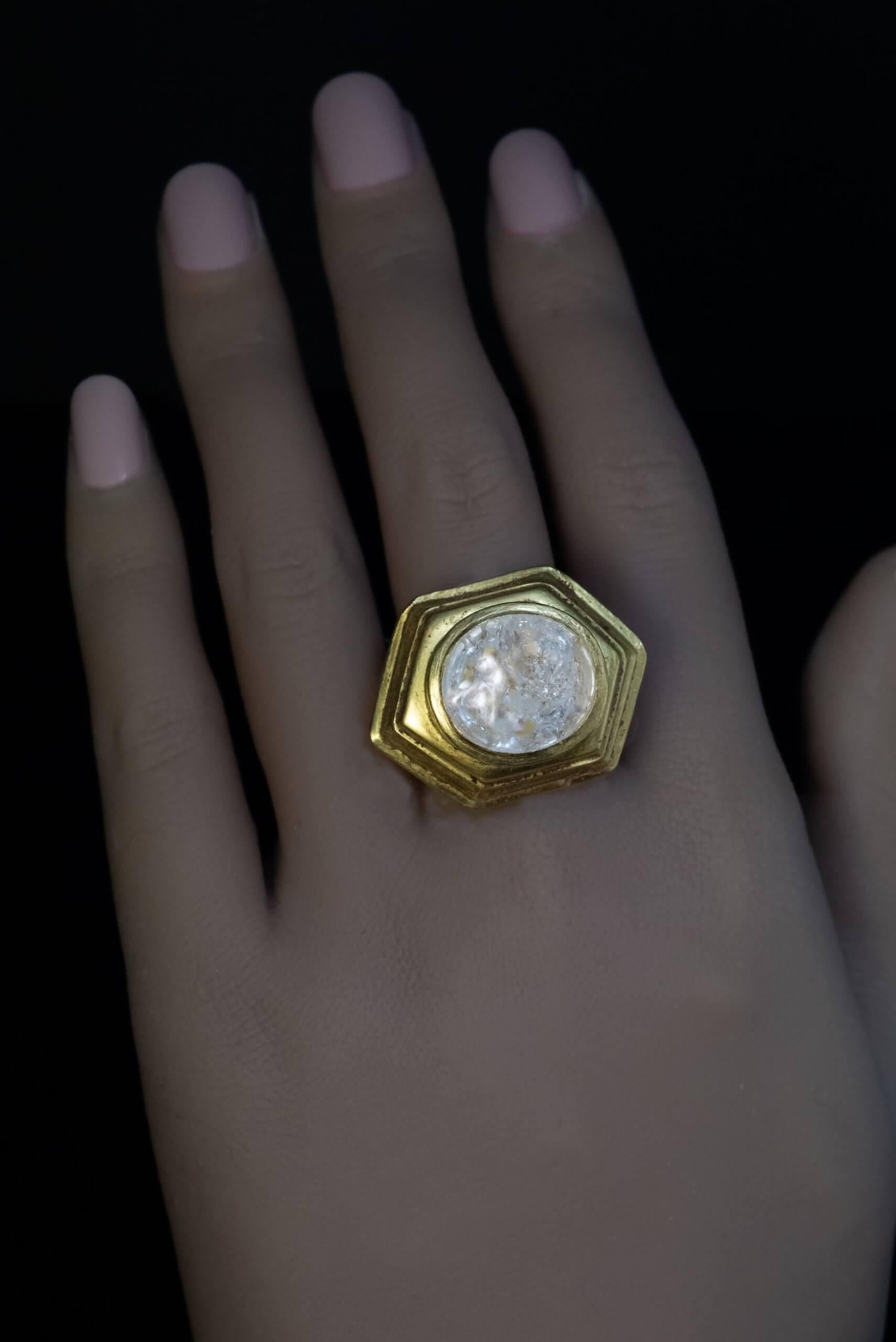 Circa 2nd century BC.  This highly unusual and heavy ancient Greek ring of a complex design is crafted in high karat gold (approximately 21.34 Kt). It features a large cabochon cut rock crystal set in a hexagonal stepped bezel. The boat-shaped shank