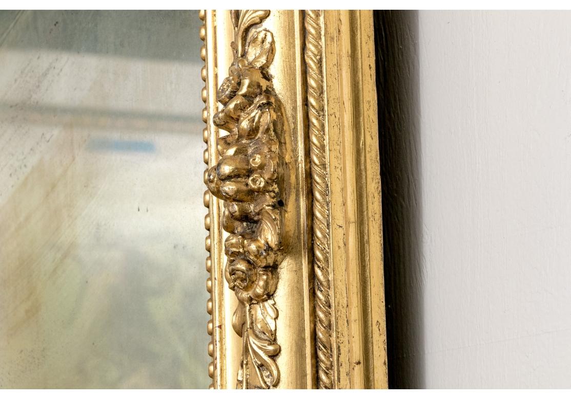 Grand miroir mural ancien de style Louis Philippe avec dessus arqué et miroir en verre au mercure. Le miroir présente des panneaux alternant des finitions brillantes et satinées, un cimier en forme de coquille flanqué de motifs floraux et de