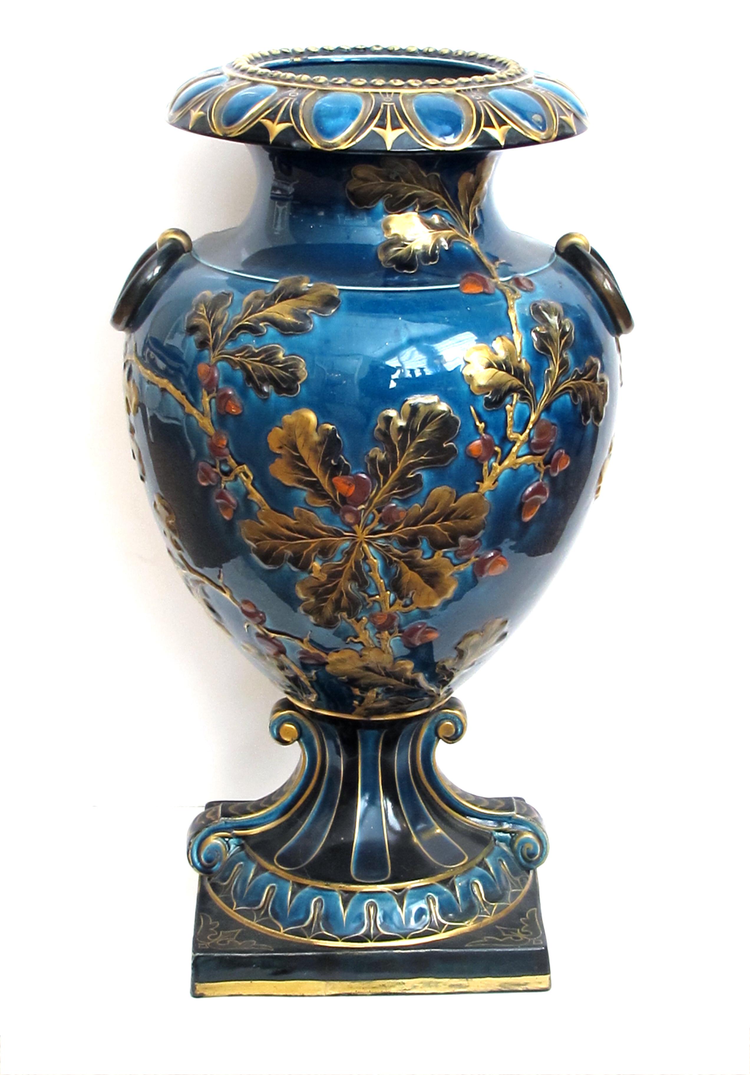 A large and exquisitely rendered English teal-glazed ceramic urn with raised oak branch-work decoration; a true state piece with rolled lip adorned with egg-and-dart motif; above an ovoid body flanked by applied ring handles and decorated with