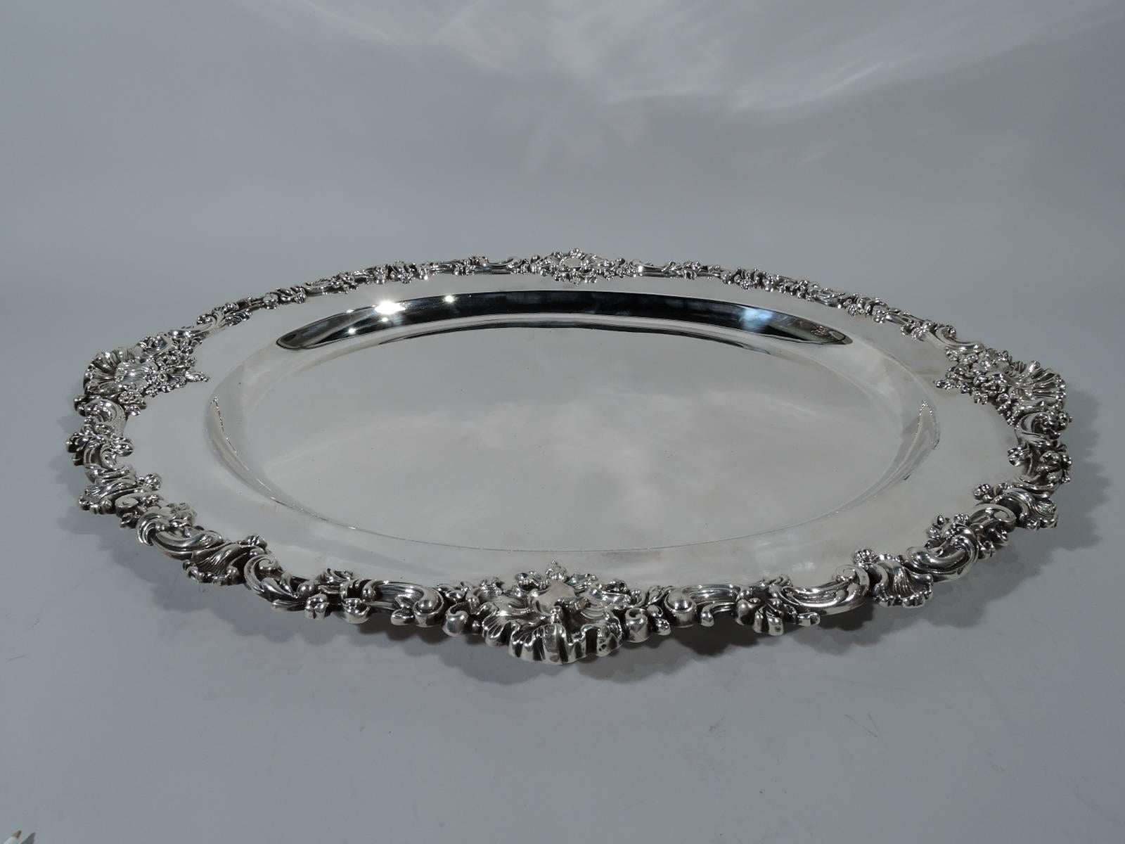 Large American sterling silver serving tray, circa 1890. Oval well and sumptuous and substantial rim with applied flowers, leaves, and shells. A piece of the fancy. Hallmarked Theodore B. Starr, a turn-of-the-century New York maker and retailer.