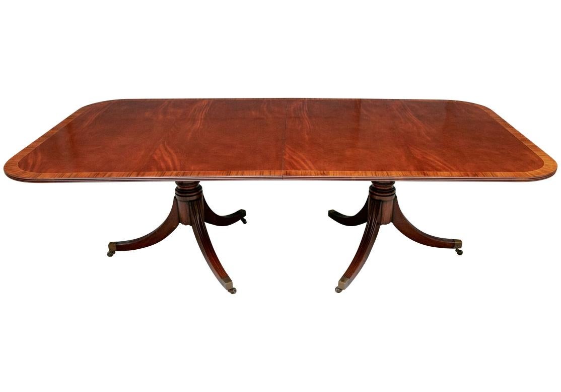 A double pedestal dining table with handsome softly grained wood  with contrasting and complementing rosewood banding with Reeded edge and having strongly formed turned pedestals and Reeded legs with simple and elegant brass caps on castors. The