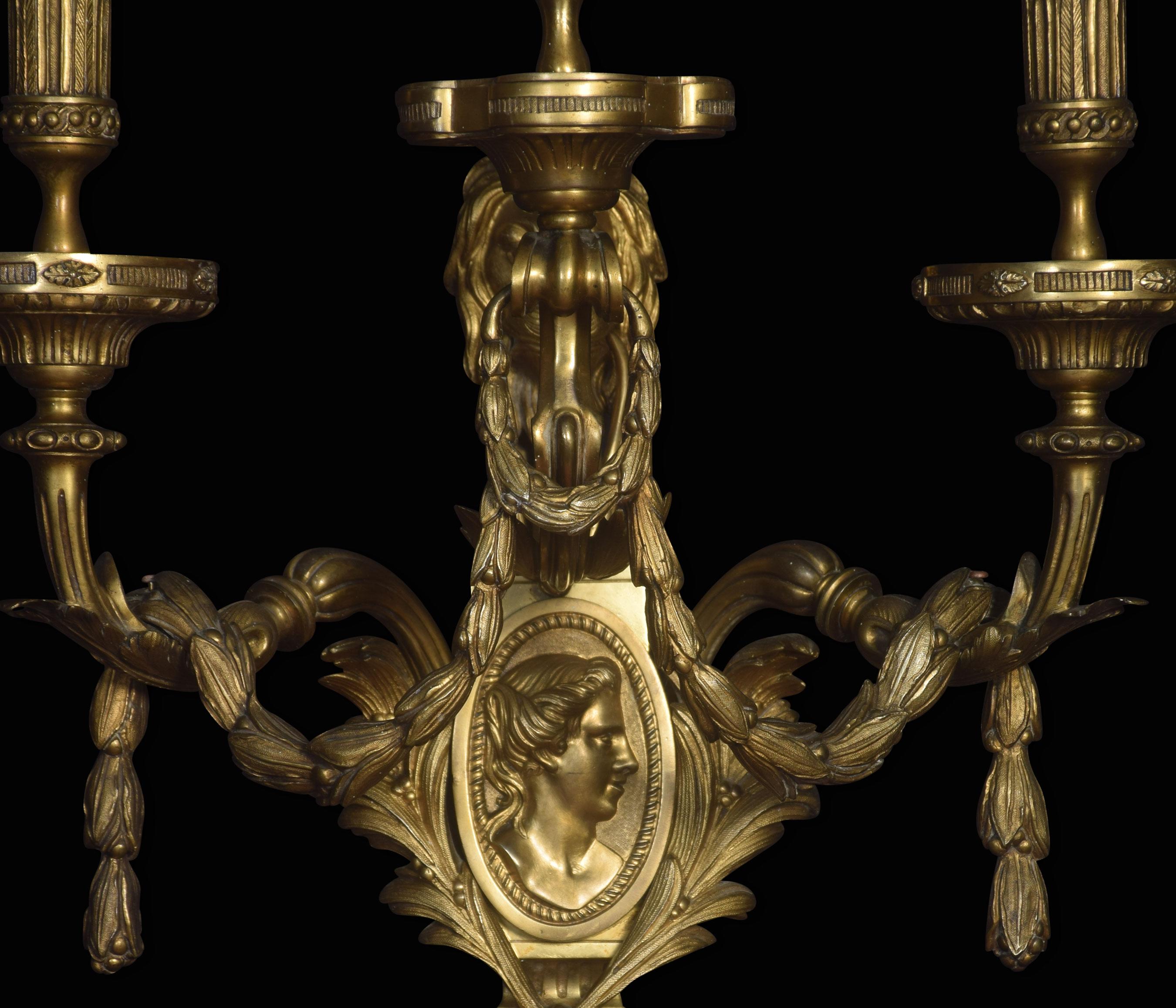 A large and impressive pair of late 19th century three-branch wall lights, each having tapering backplate with central oval profile medallion and lion mask finial issuing three acanthus leaf branches hung with husk swags. Converted for