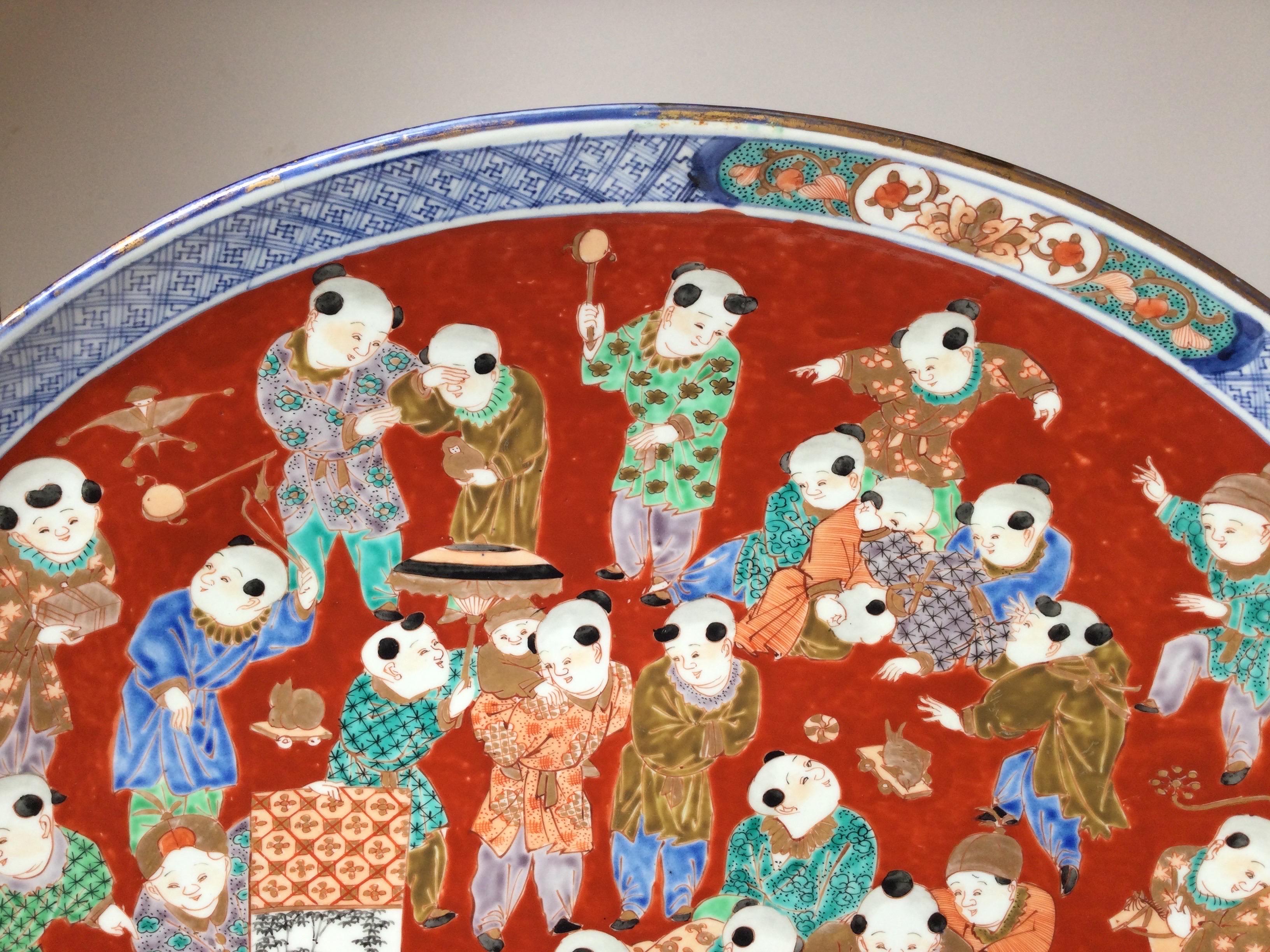 A large 22 inch diameter porcelain charge, Japan, 1880's. The unique and vibrant decoration of Japanese children playing, all in elegant brightly colored robs. The red and blue main colors of Imari Porcelain.