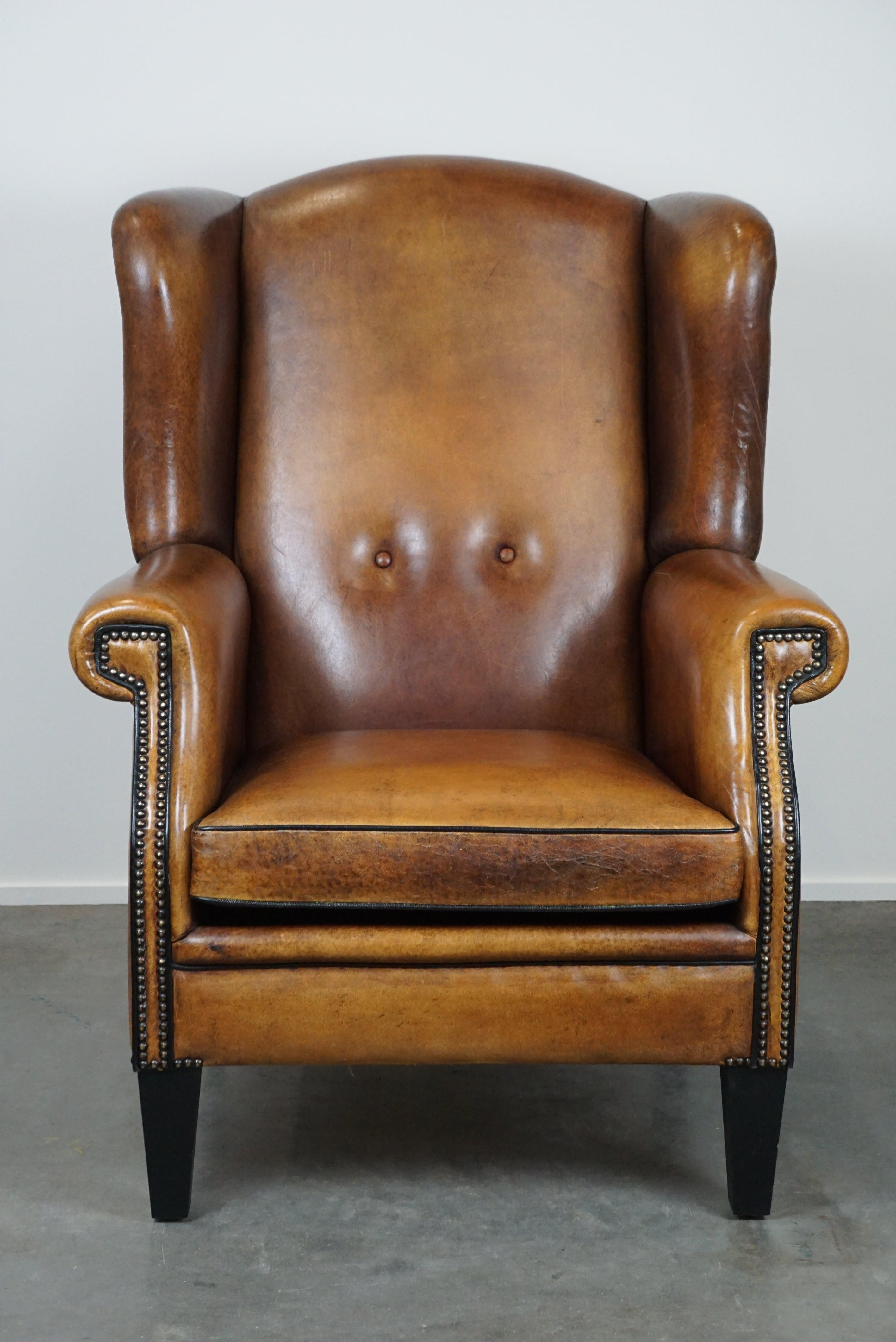 Offered is this large and very comfortable wingback armchair made of premium sheep leather and finished with a luxurious nail and black piping combination. This beautiful large and very comfortable sheep leather wingback armchair has acquired a