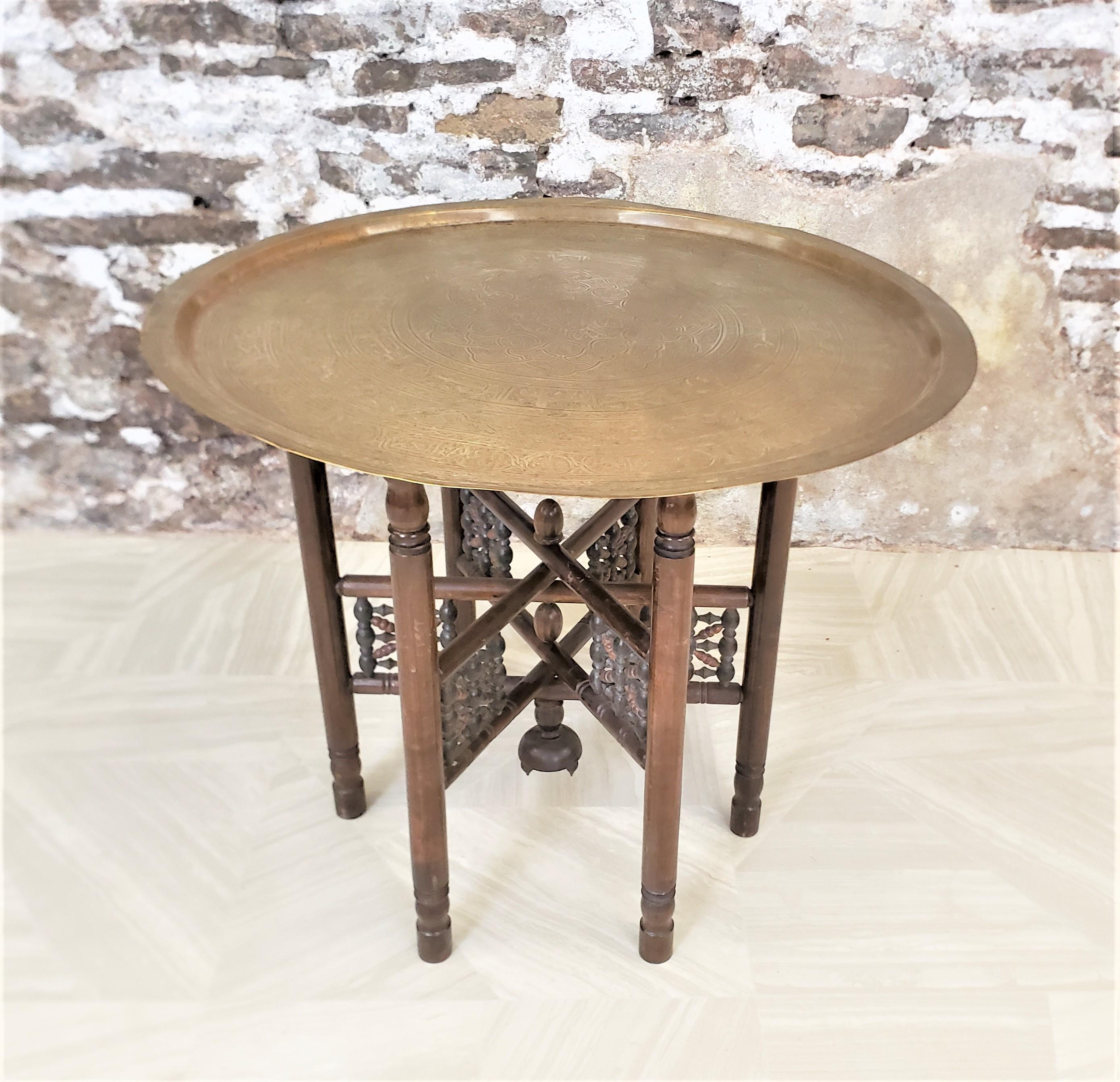 This large brass tray table has no maker's marks, but is presumed to have originated from India and dating to approximately 1920 and done in an Anglo-Indian style. The large tray has a raised rim and an engraved tray surface with detailed engraving