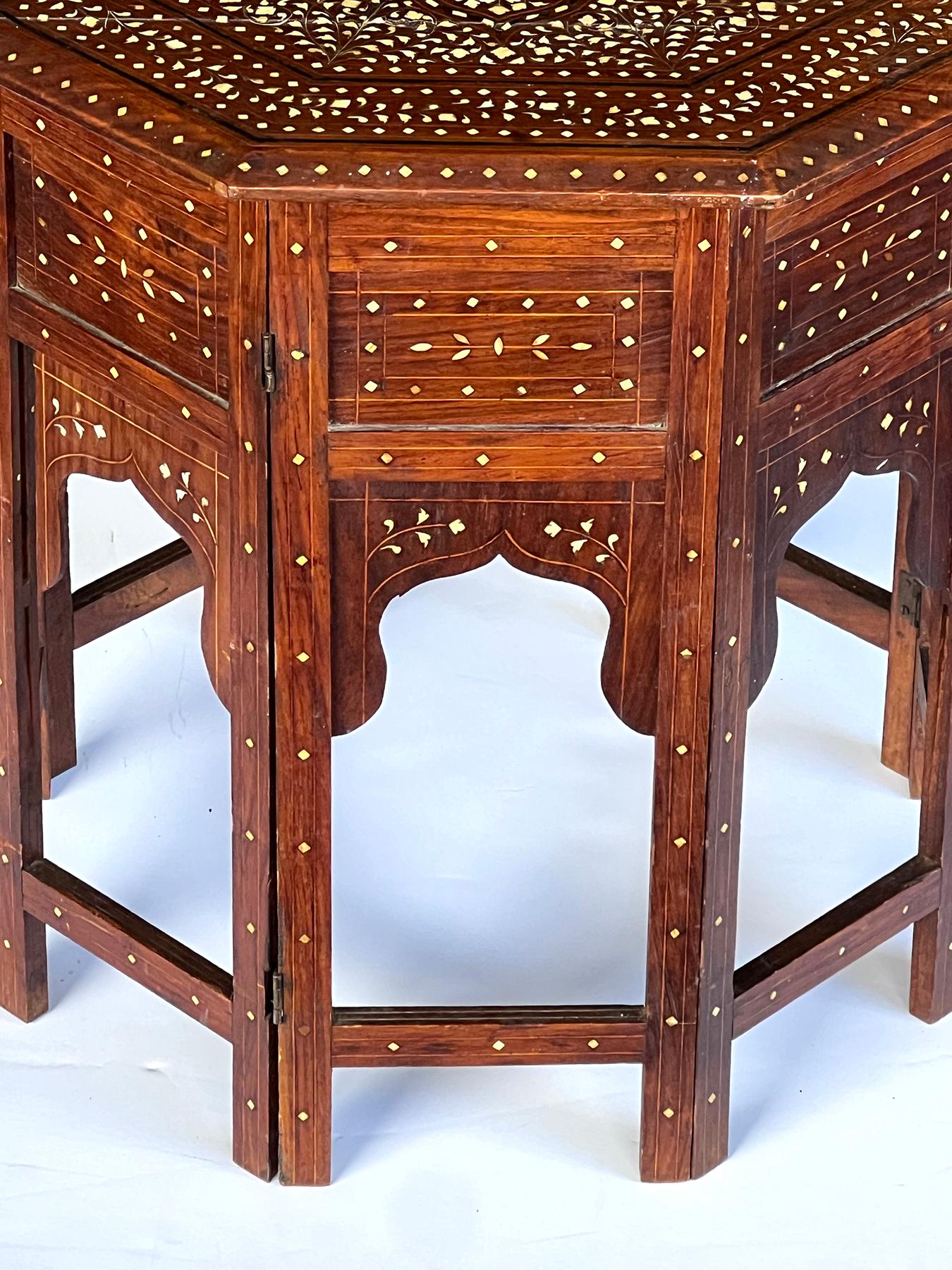 originally used as traveling tea tables for the British in India; the octagonal top centering a large stylized floral medallion surrounded foliate stems all within a preimeter border of a meandering foliate vine; raised on a hinged base with