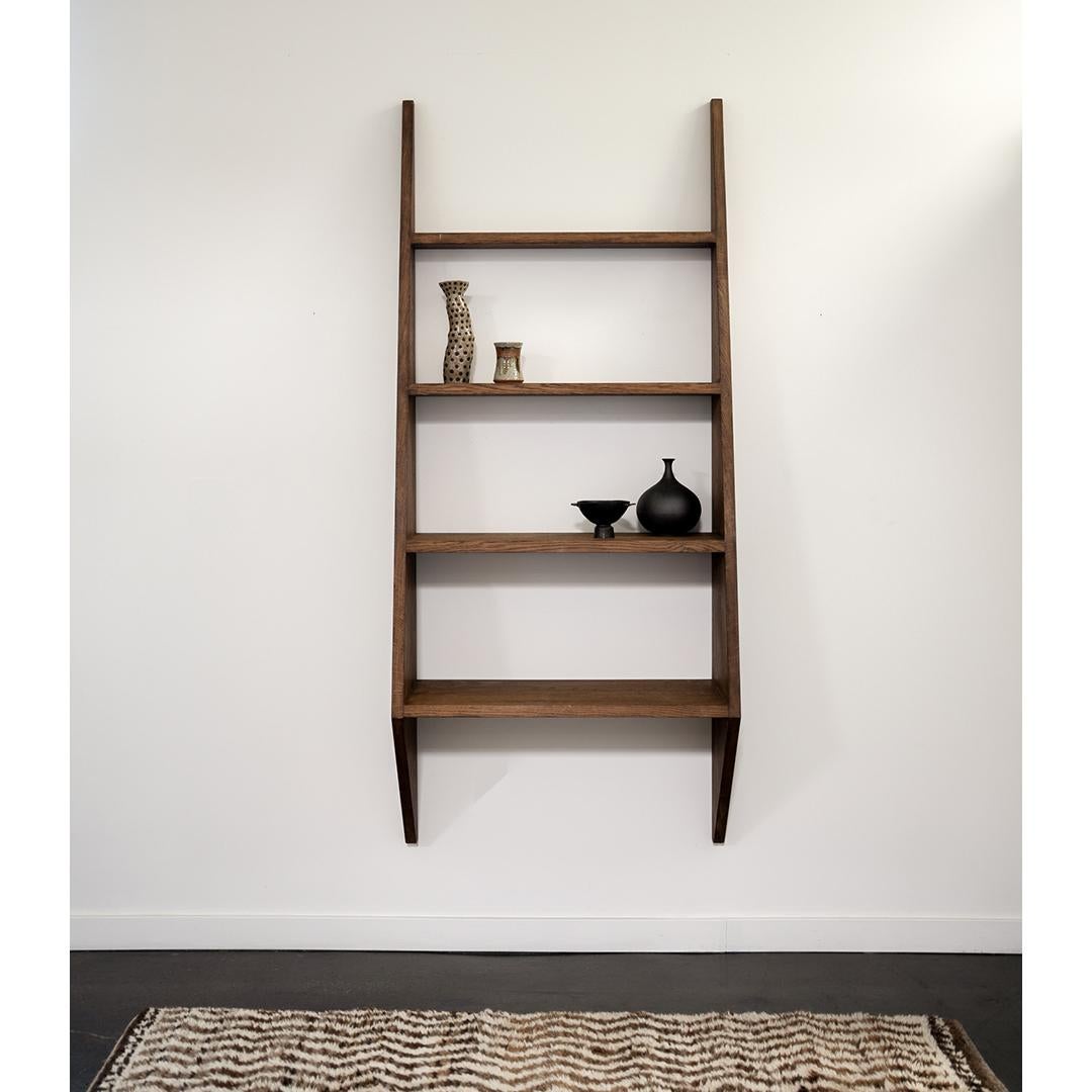 Striking in silhouette and generous in scale, this angular French bookcase is a sculptural take on classic wall-mounted shelving. Crafted in solid wood with a warm finish, the design features sharply tapered sides and five fixed shelves that vary