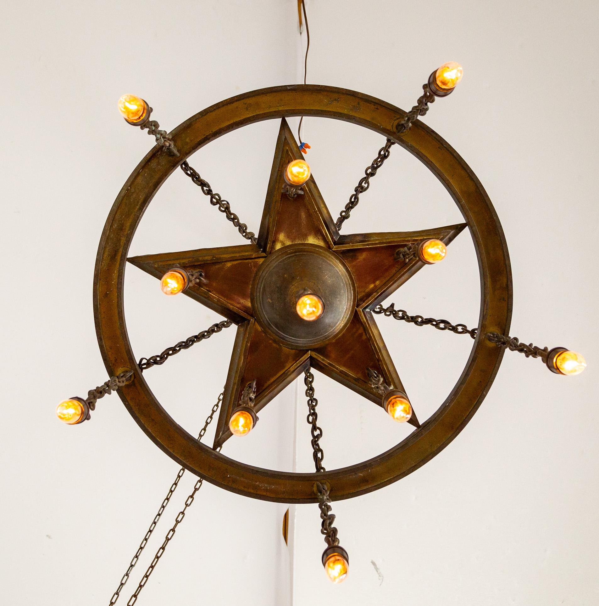 Un grande lampadario rustico con luci sospese a doccia strutturato con una stella di metallo rivolta verso il basso in un anello con catene a cascata.  Un pezzo d'antiquariato ben realizzato con grandi proporzioni e 11 luci.  Recentemente restaurato