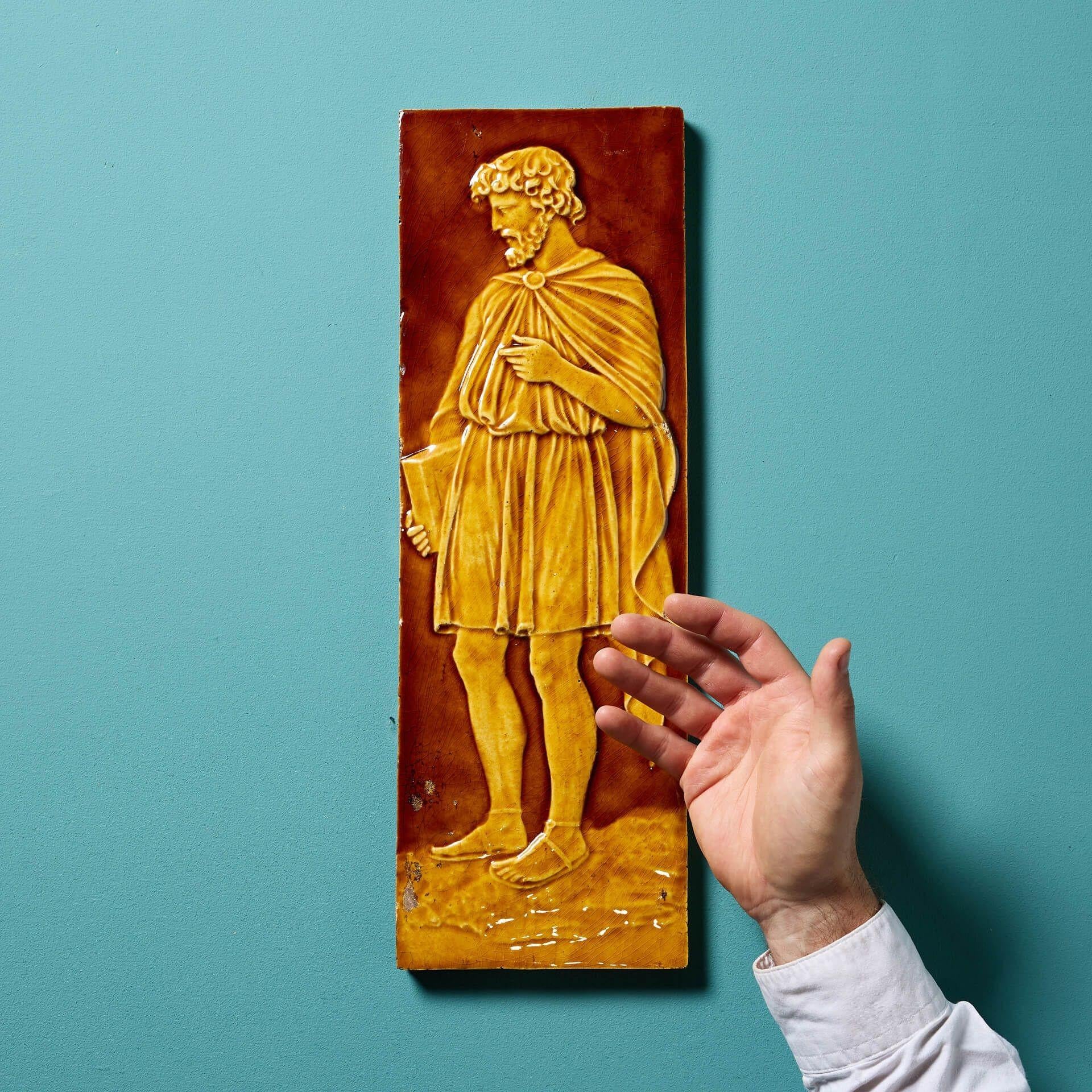 Una grande piastrella antica del XIX secolo attribuita a Burmantofts.

Modellata in rilievo, questa piastrella da 15 cm di diametro mostra uno studioso maschio vestito in modo classico e smaltato in tonalità ocra e melassa.

Risalente al 1880 circa,