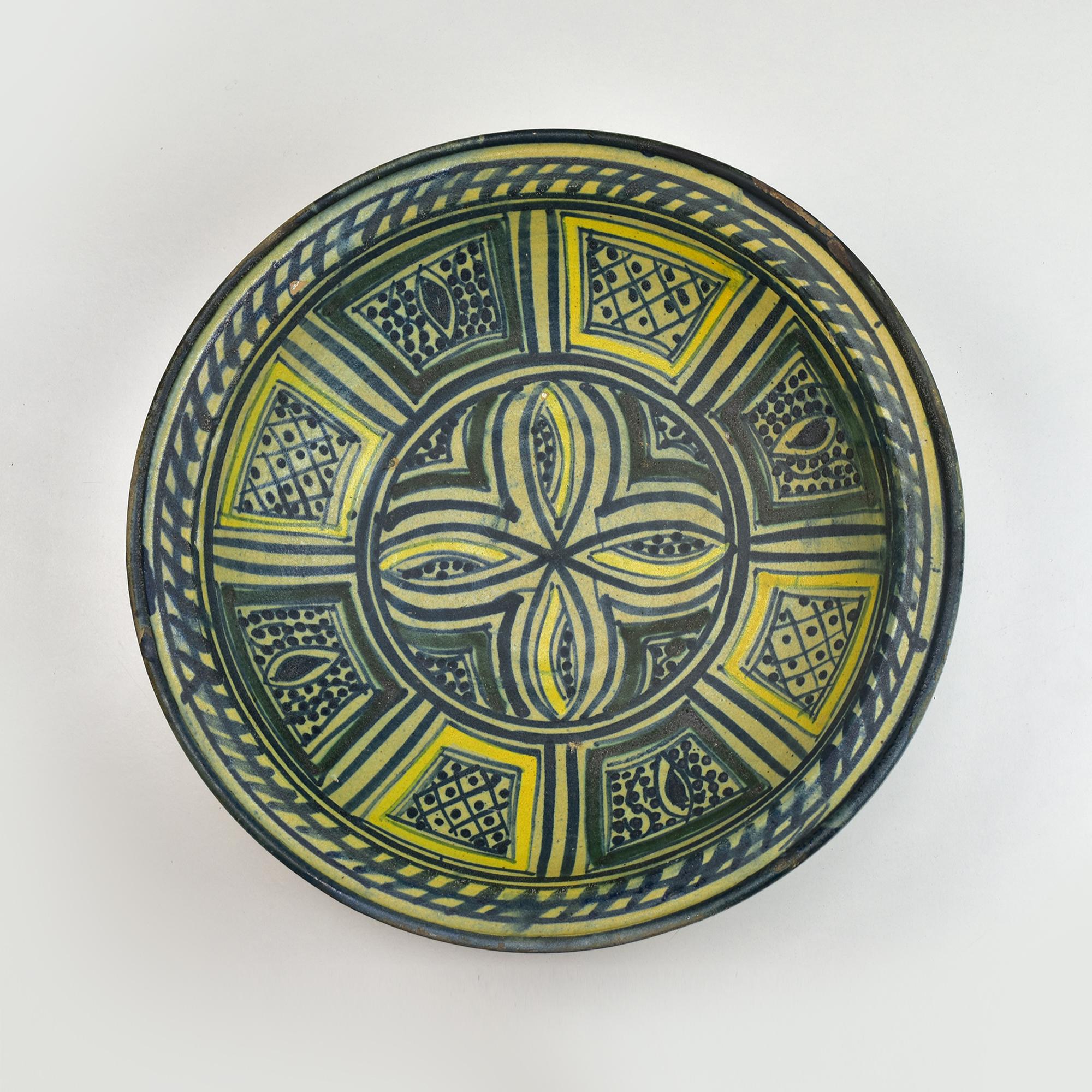 This exquisite 19th-century Moroccan ceramic bowl from Fez showcases traditional craftsmanship with its vibrant polychrome decoration. The bowl features an intricate geometric and floral design rendered in shades of deep blue, green, and yellow,