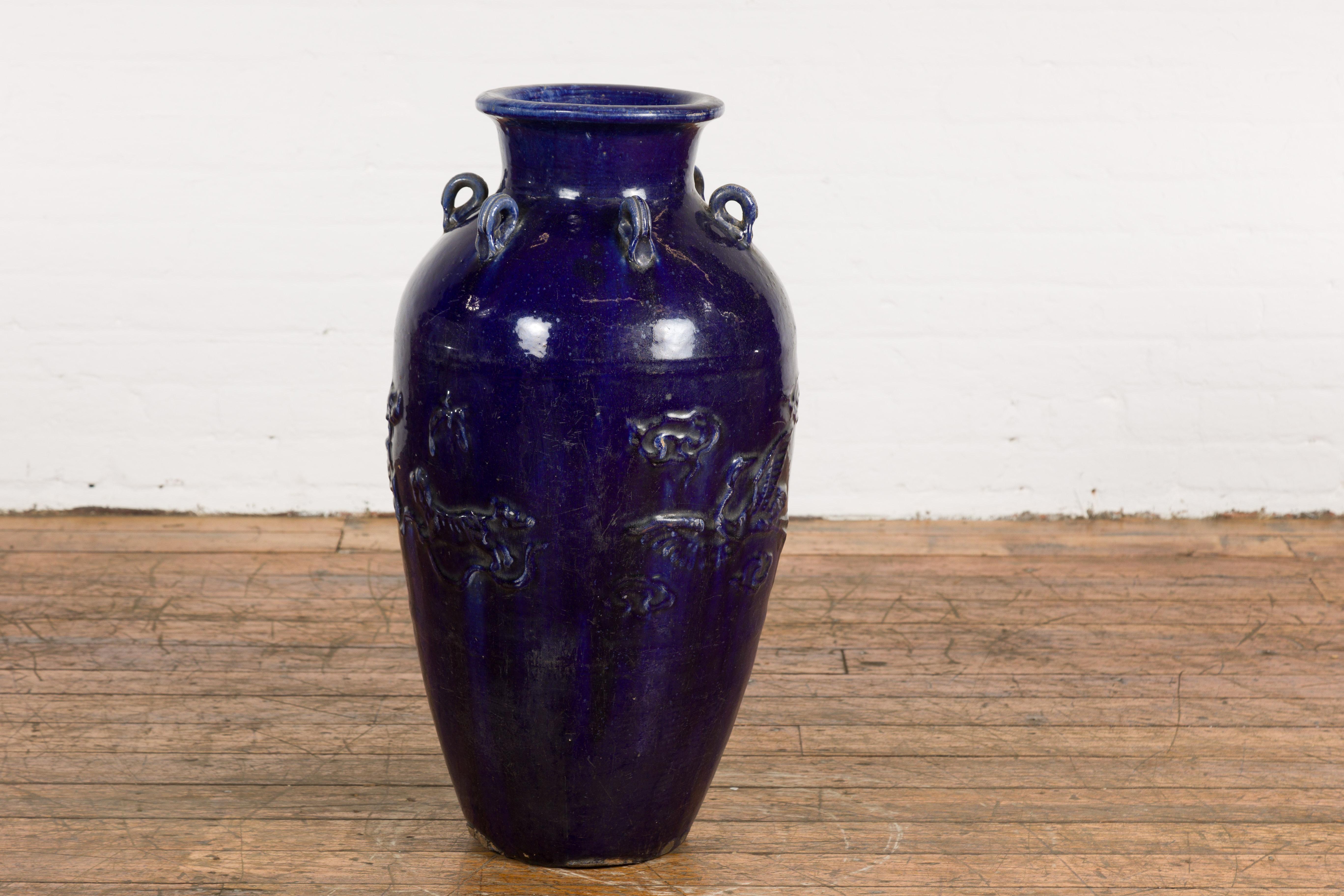 An antique Thai large cobalt blue glazed Martaban jar from the 19th century, with petite swan neck loops, raised birds and tiger motifs and tapering lines. Created in Thailand during the 19th century, this large Martaban vase attracts our attention