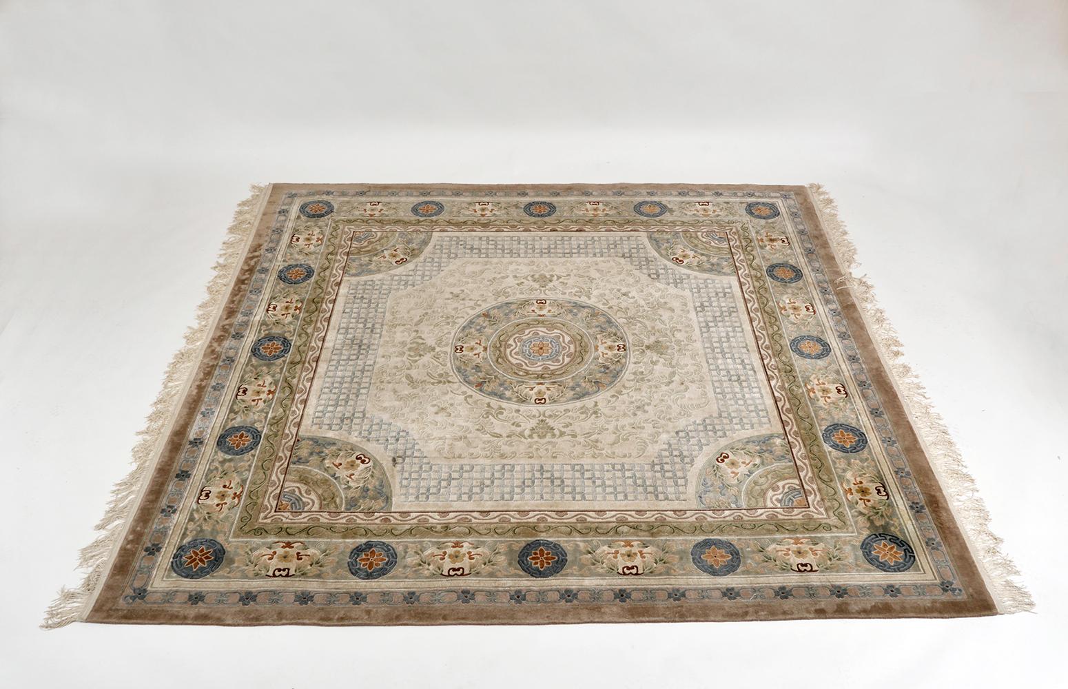 A very attractive and large Chinese silk rug with central floral motif and stylised linked chain lattice in subtle colours depicting lotus flowers, symbols of wealth and foliage on a cream background with muted browns, blues, greens and rust colours