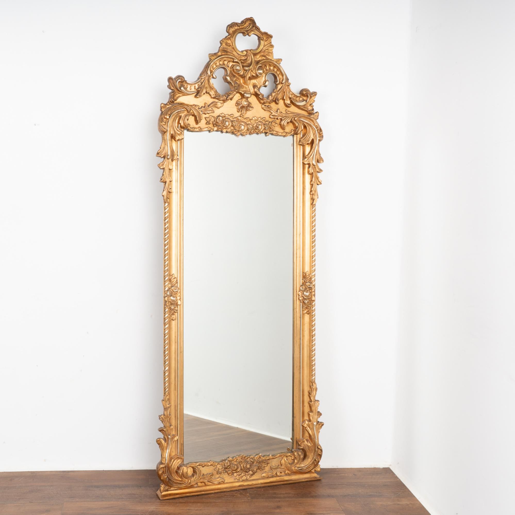 This stunning 7' gold gilt mirror is crowned with carved flowers and flourishes. The sides and lower corners/bottom are accented with refined effect.
There is expected age-related wear as seen where the gilt has been worn off, chipped or multiple