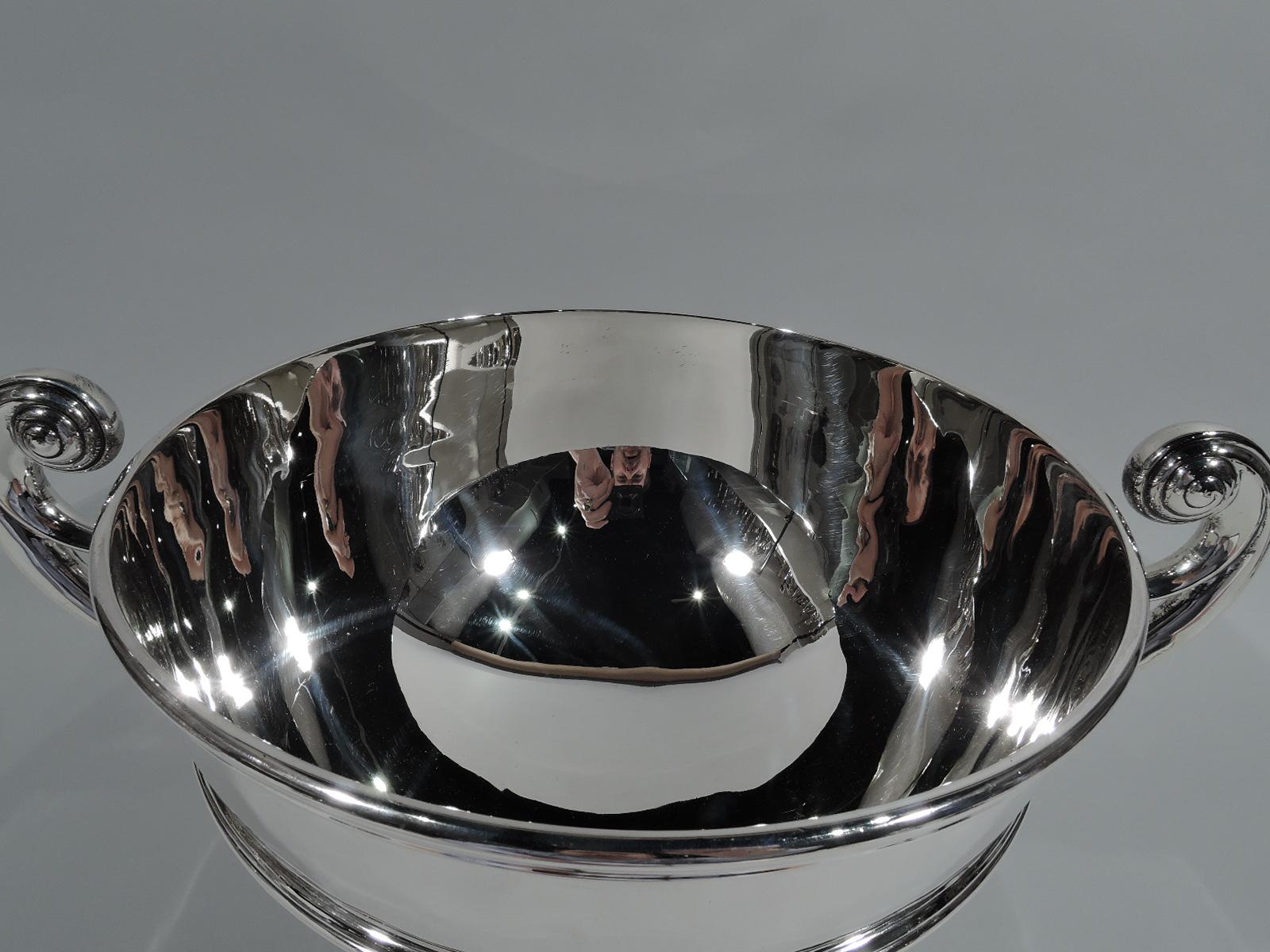 Large Edwardian Classical sterling silver trophy bowl. Made by Durgin (part of Gorham) in Concord, New Hampshire, ca 1900. Round and girdled bowl with capped and flying double-scroll handle, molded rim, and stepped foot. Substantial with nice heft