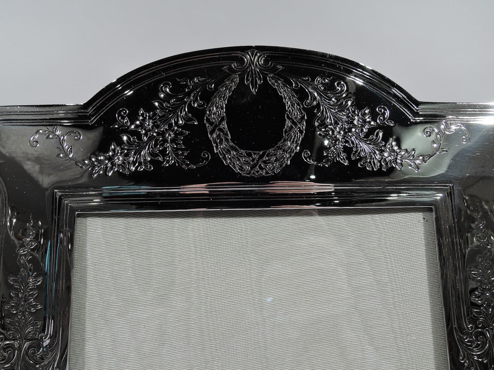 Large turn-of-the-century Edwardian Regency sterling silver picture frame. Made by Durgin (part of Gorham) in Concord, New Hampshire. Rectangular window in shaped surround with straight sides, bracket feet, and arched top. Engraved garlands and