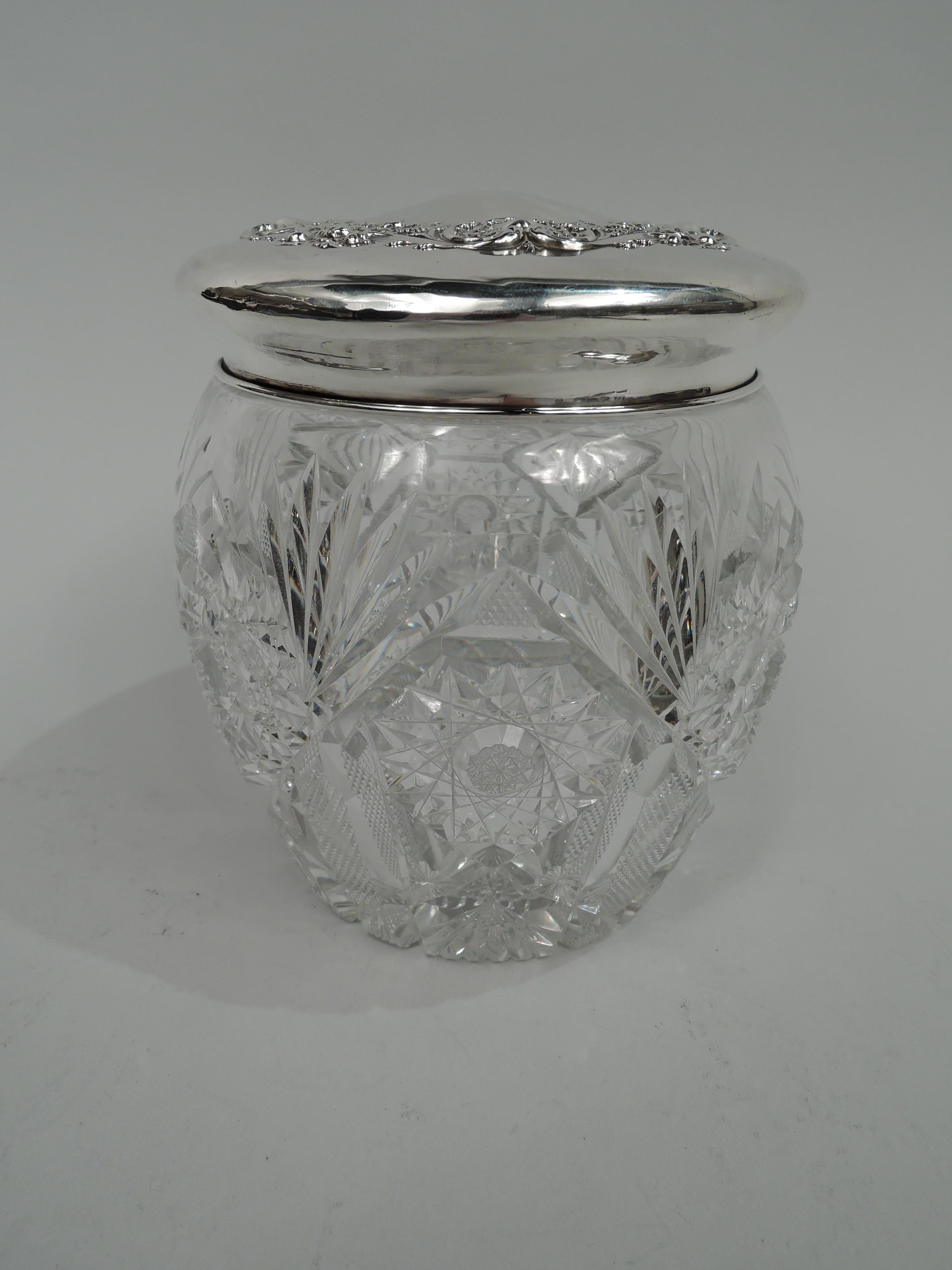 Large brilliant-cut jar with sterling silver cover. Made by Watson Co. in Attleboro, Mass., ca 1900. Round and curved with stars, ferns, and diaper. Cover gently raised; on top repousse shell, scroll, and flower wreath (vacant center). Cover