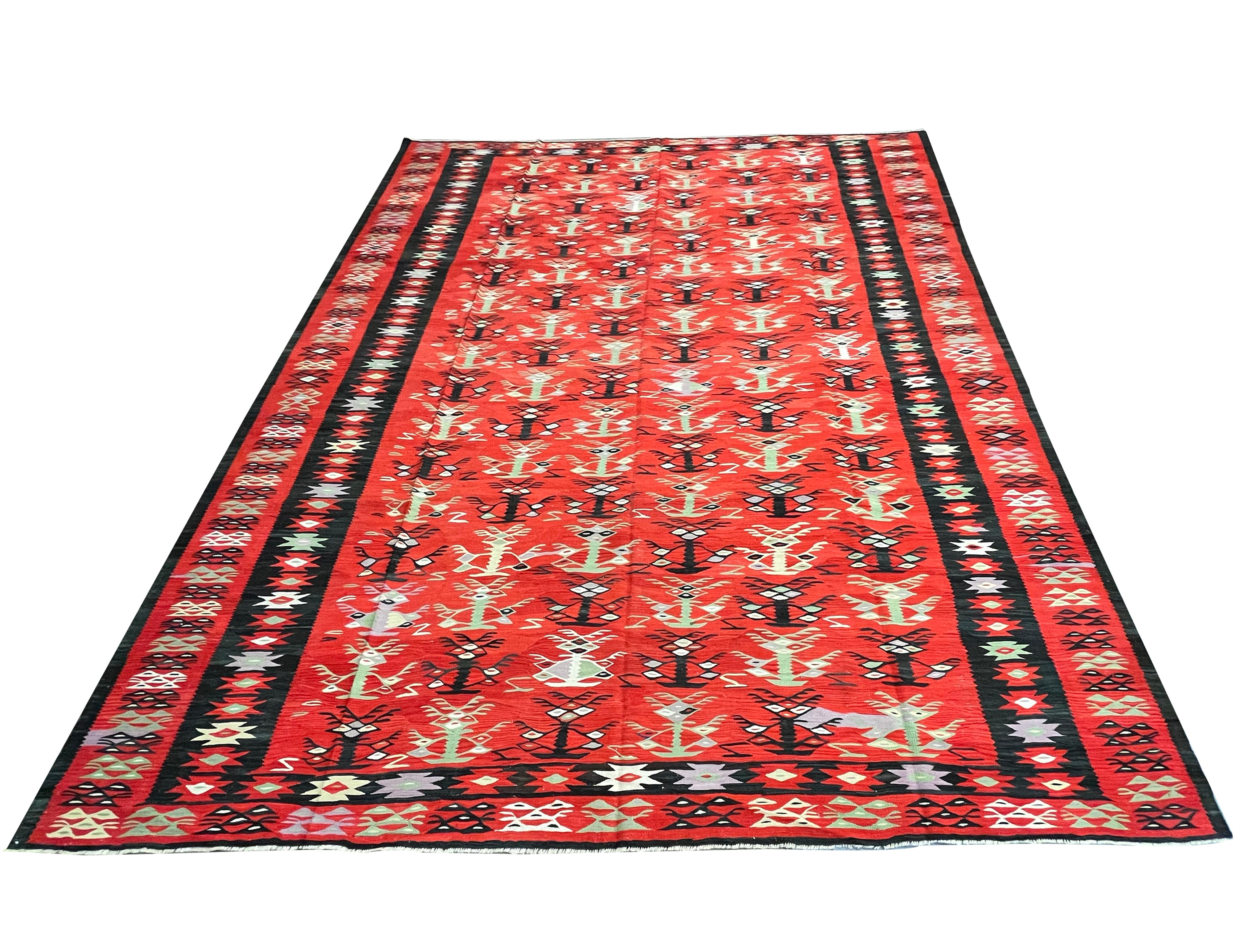 This bold red kilim is a traditional flatwoven area rug woven by hand circa 1900. The design features a geometric design woven in bold black, green, and blue accents on a beautiful red background. The stripe design is eyecatching, so this piece is