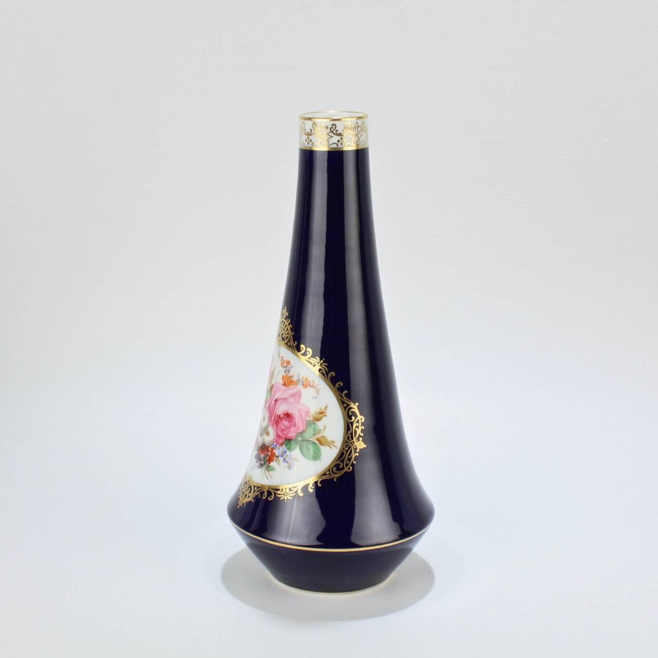 A fine Meissen porcelain vase with a cobalt blue ground, floral spray in a central cartouche, and gilding throughout. 

The vase has an elegant, Art Nouveau form with a long, tapered neck that flares outward to an inverted trumpet form, which
