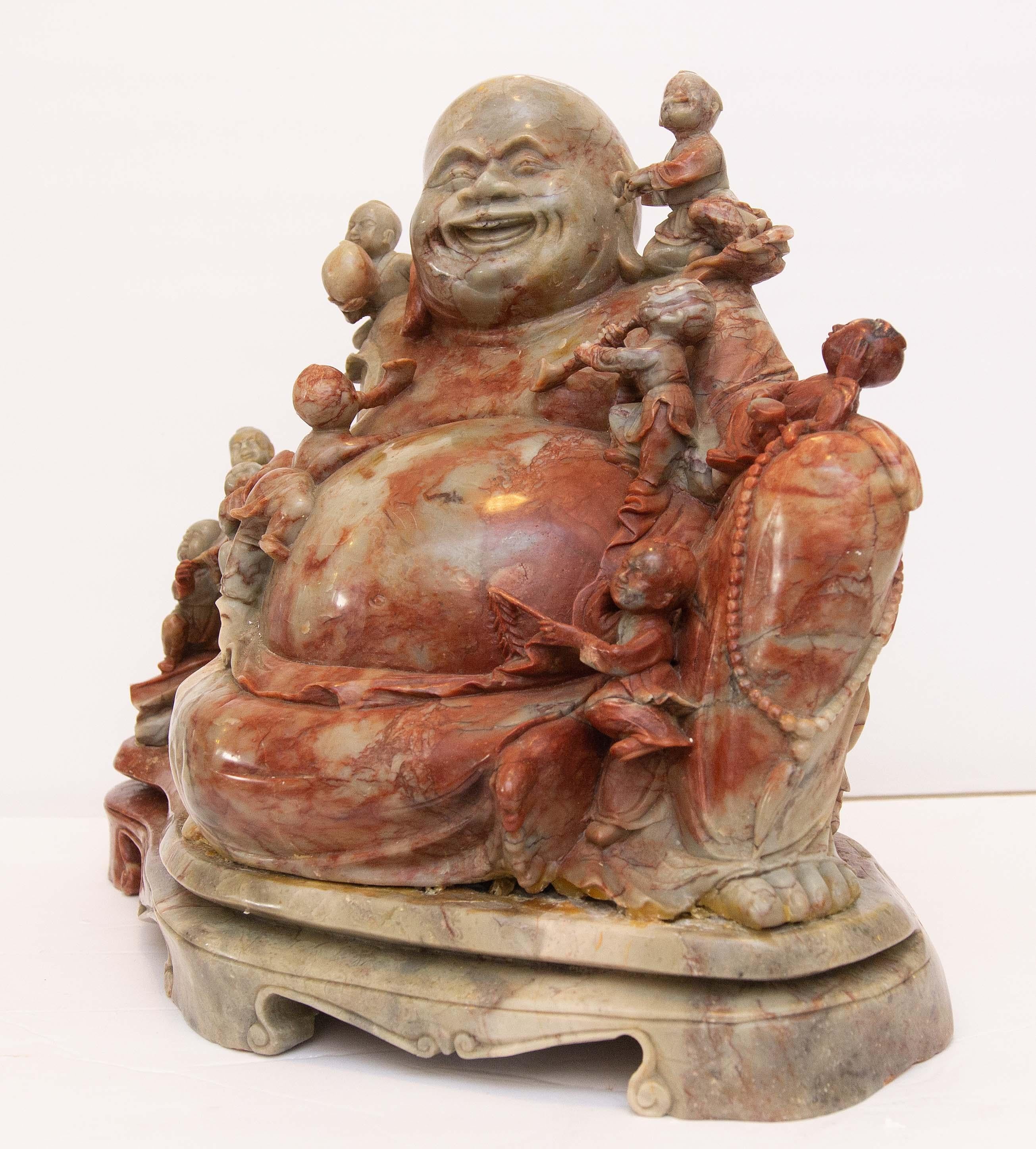 Large Chinese soapstone sculpture of a laughing Buddha. He is surrounded by children playing music and bearing gifts. 20th century.
