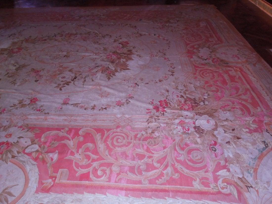 Large Aubusson rug with a floral motif in apricot, coral and pink. Coral and apricot borders a floral design on a cream ground. Small tears scattered throughout.
