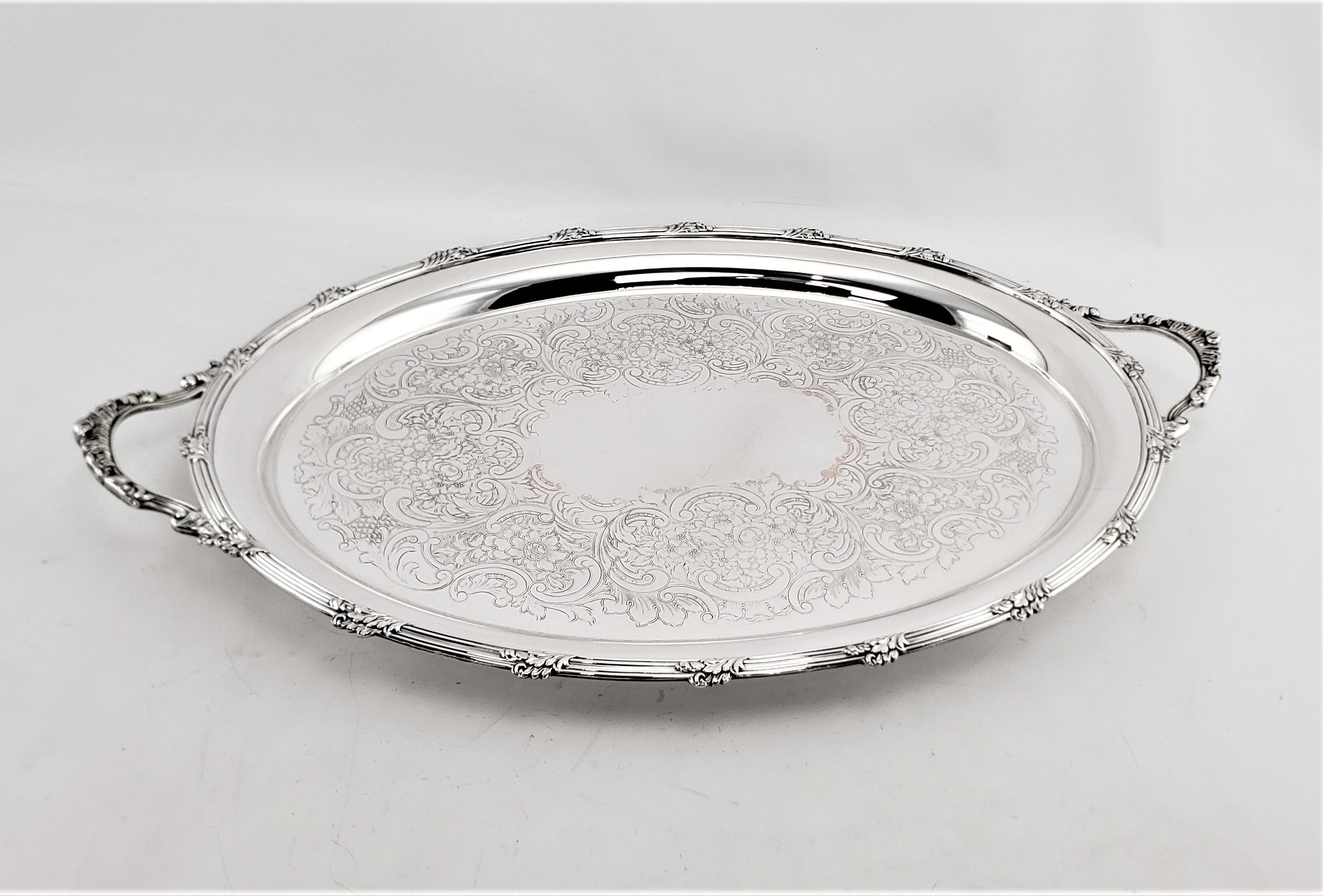 This very large oval silver plated serving tray was made by the renowned Barker-Ellis Silver Co. of England in approximately 1920 in an Edwardian style. The surface of the tray is ornately engraved with a scrolling floral motif, which is accented by