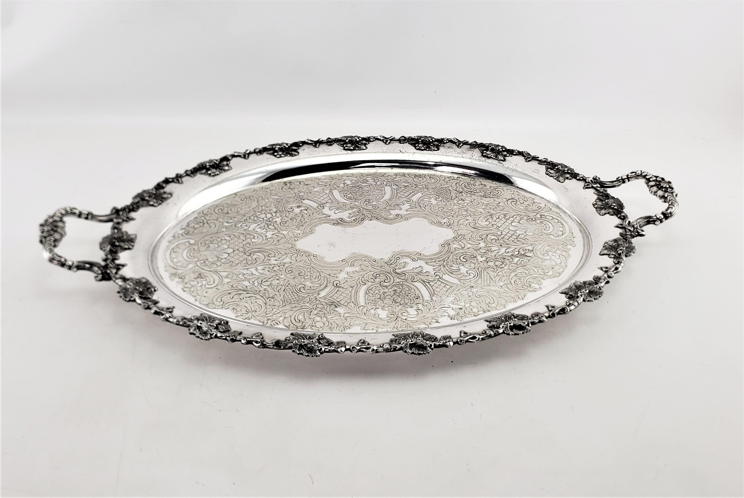 This large antique oval silver plated serving tray was made by the renowned Barker-Ellis Silver Company of England is approximately 1900 in a Victorian style. This oval tray is adorned with ornate applied decoration of leaves and berries which is