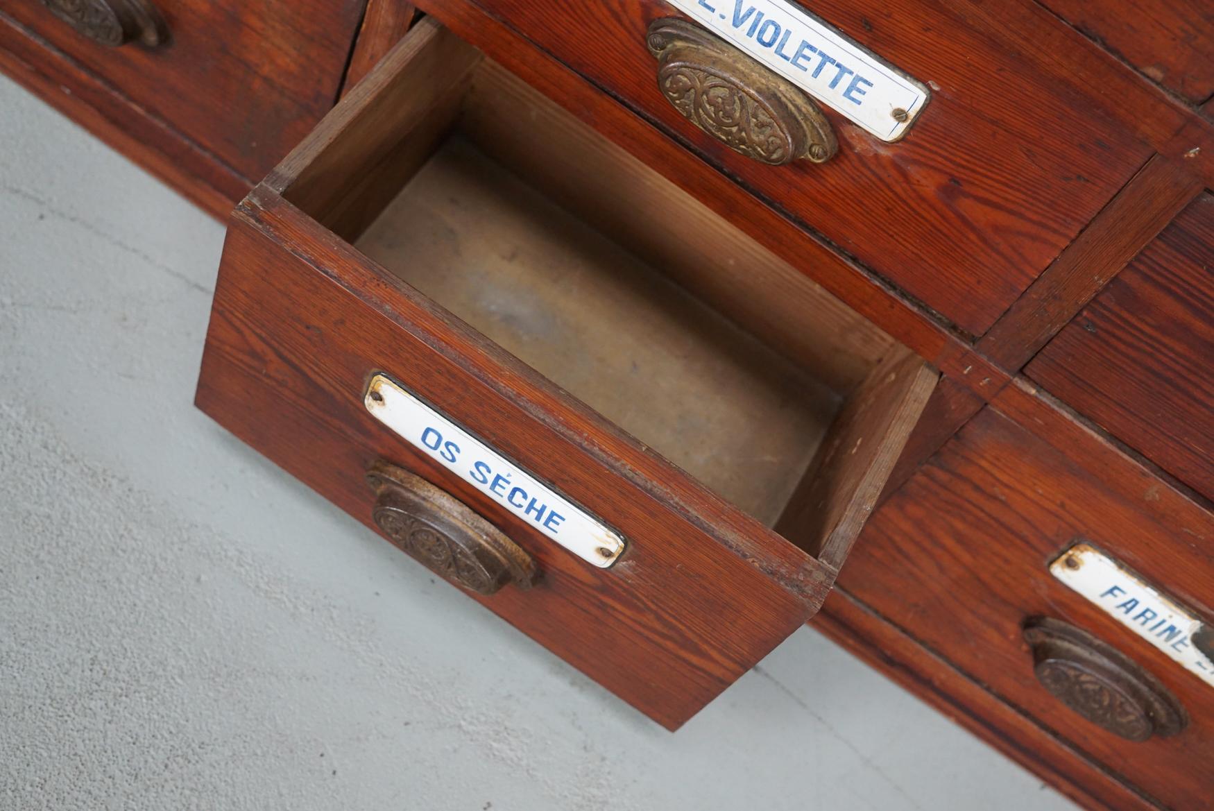 This apothecary bank of drawers was designed and made circa 1900 in Belgium. It was made from pitch pine with cast iron art nouveau style handles and enamel name plates for the contents. The cabinet has retained a rich patina with some natural