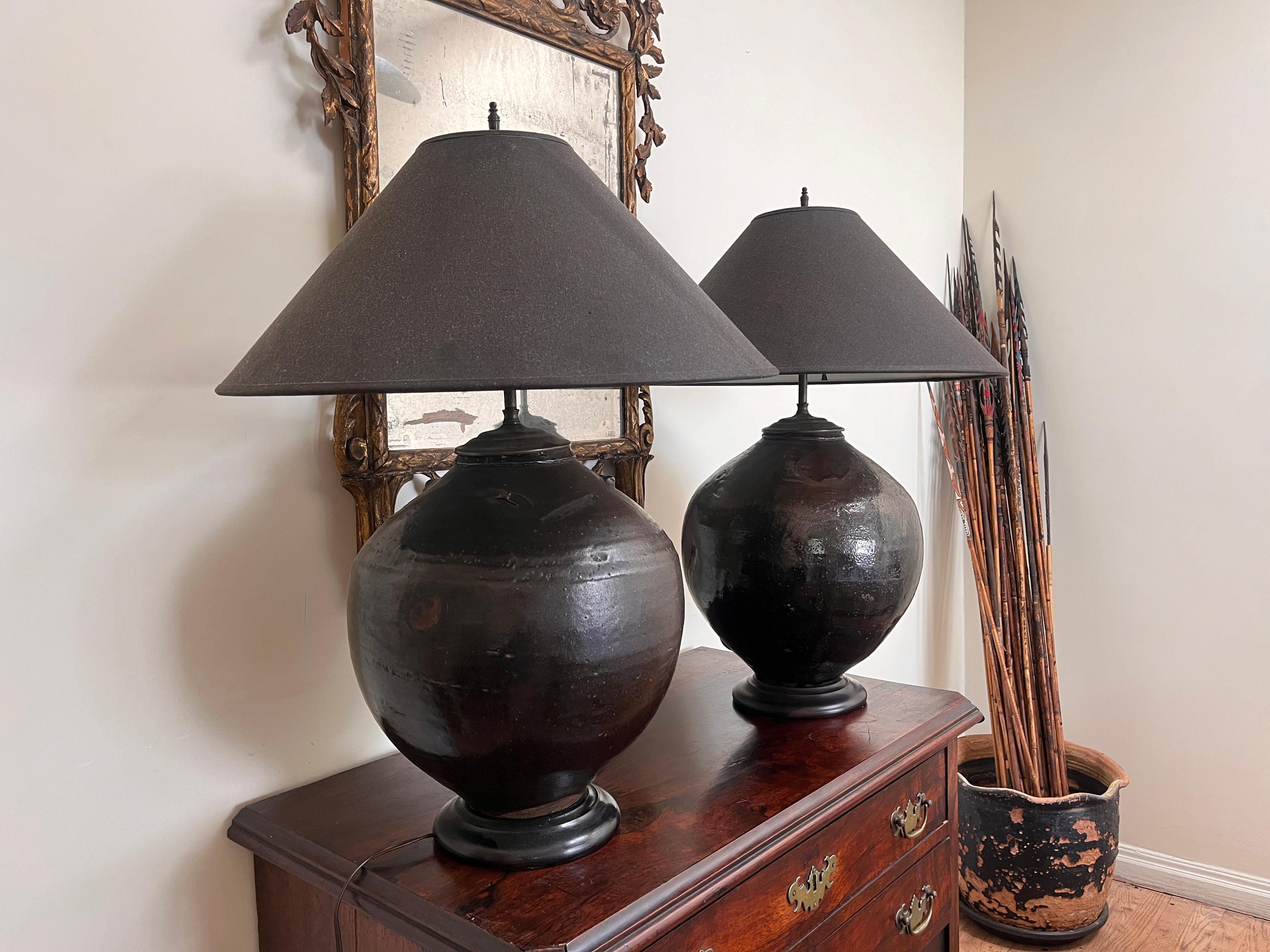 Large pair of black-glazed antique clay jar pots on a wood base with RH shades.