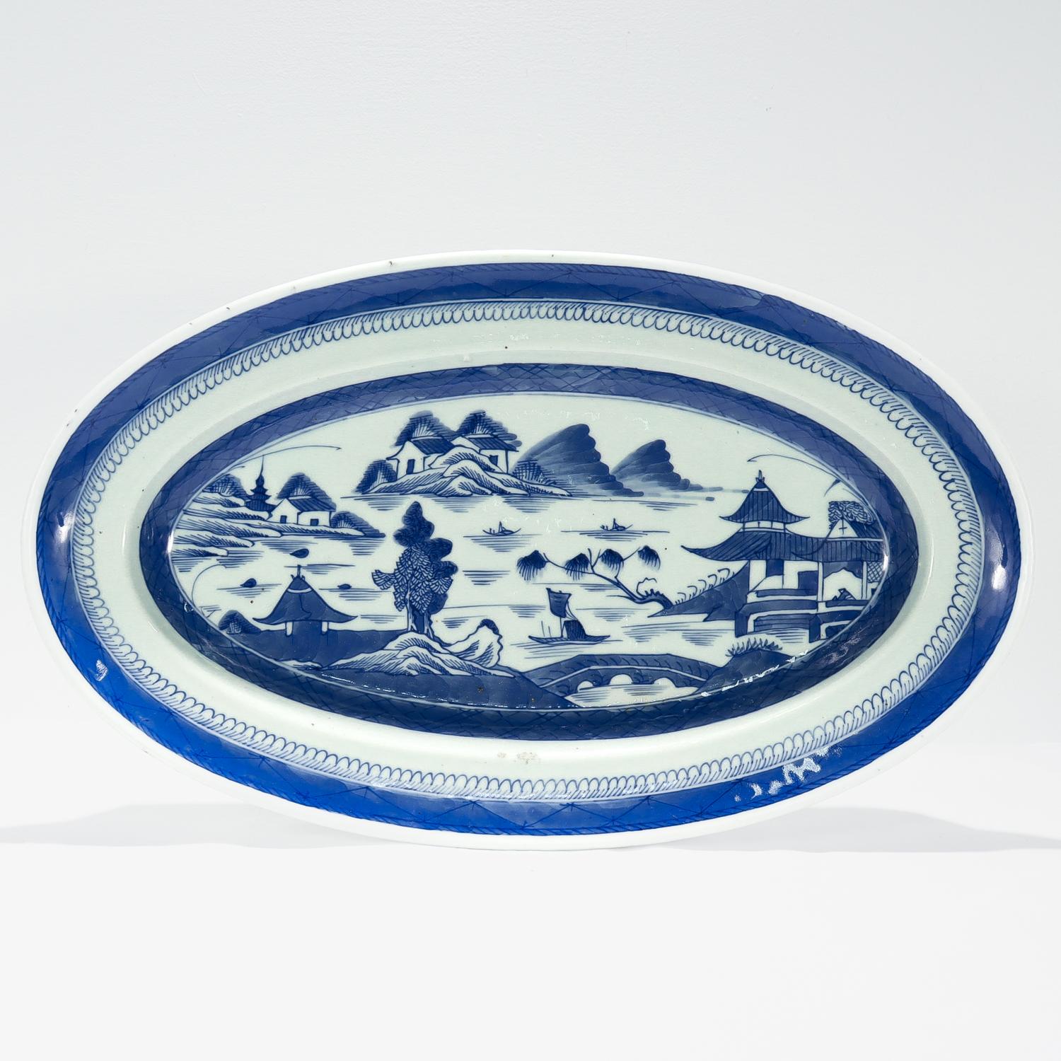 A large fine antique Chinese export porcelain serving tray.

In the Canton pattern.

Decorated in underglaze blue.

Depicting a mountainous Chinese village to the top of the lid and the long sides of the body. The background has houses, mountains,