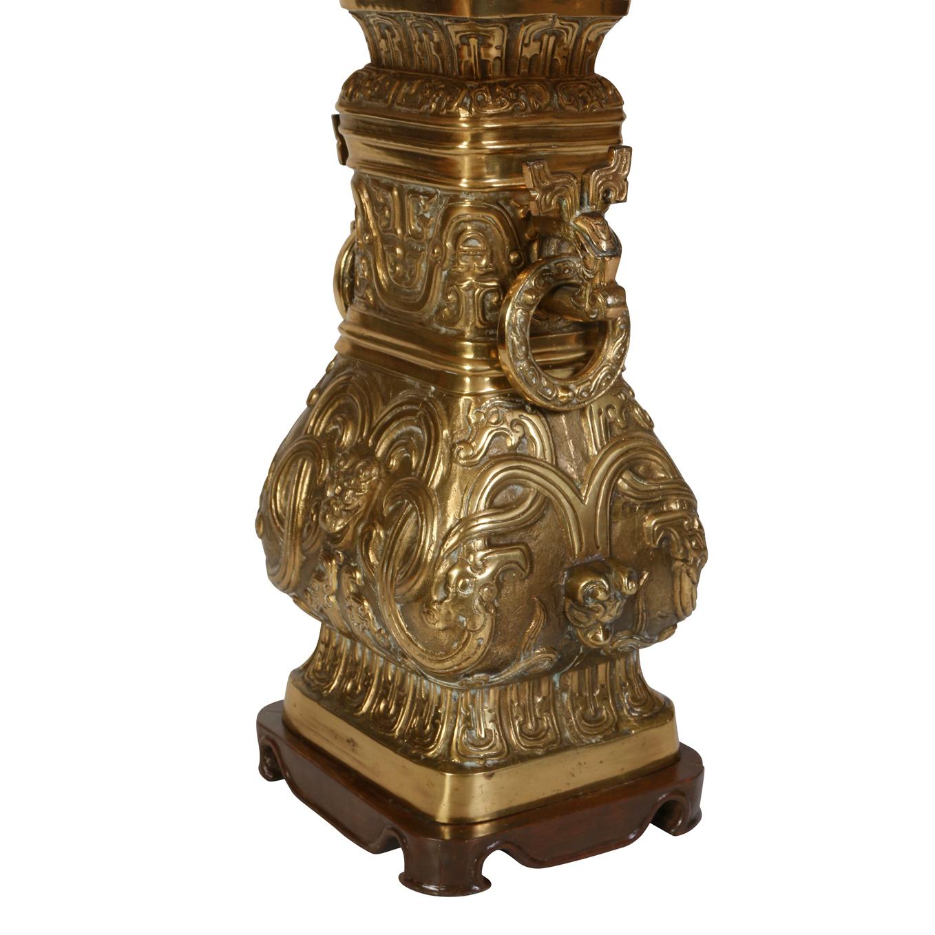 An antique bronze Asian lamp with two ring handles and raised relief detail on all sides set on a wood base.