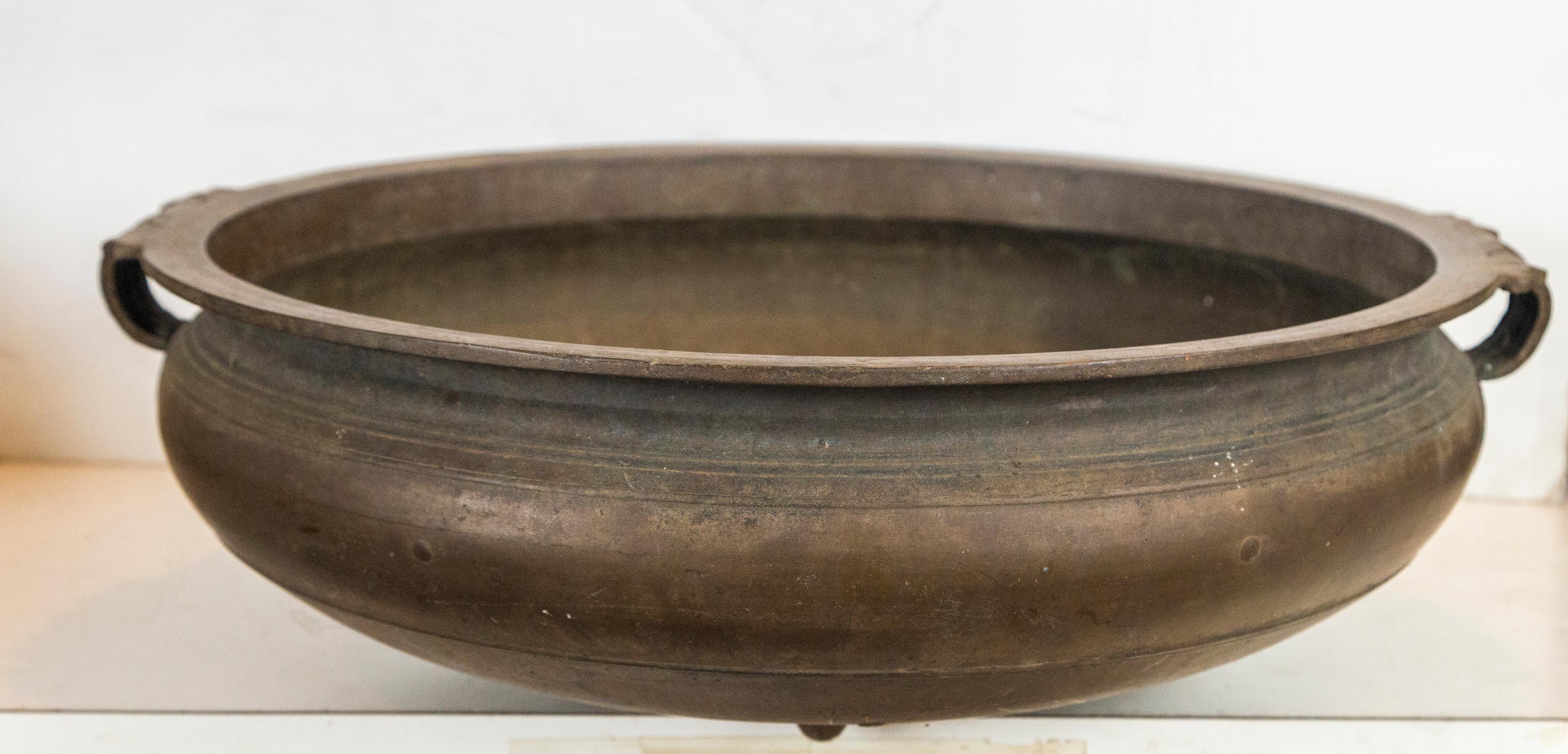 Indian cast bronze urli of shallow circular form. Probably cast using the lost wax technique, These urlis were a traditional container used for serving food in temples and other holy sites. Scrolling handles from the rim, above a decorative element.