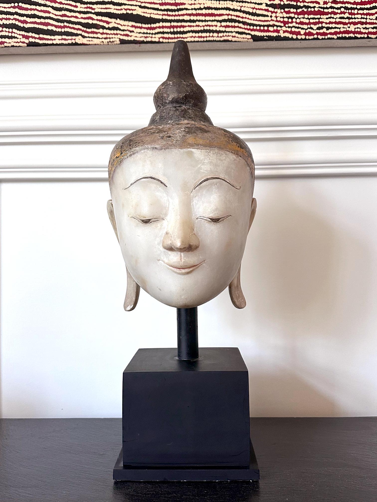 Una grande statua a grandezza naturale della testa di Buddha scolpita da un unico blocco di marmo alabastro bianco e dipinta con pigmenti d'oro e neri. La scultura era di un iconico stile birmano 
