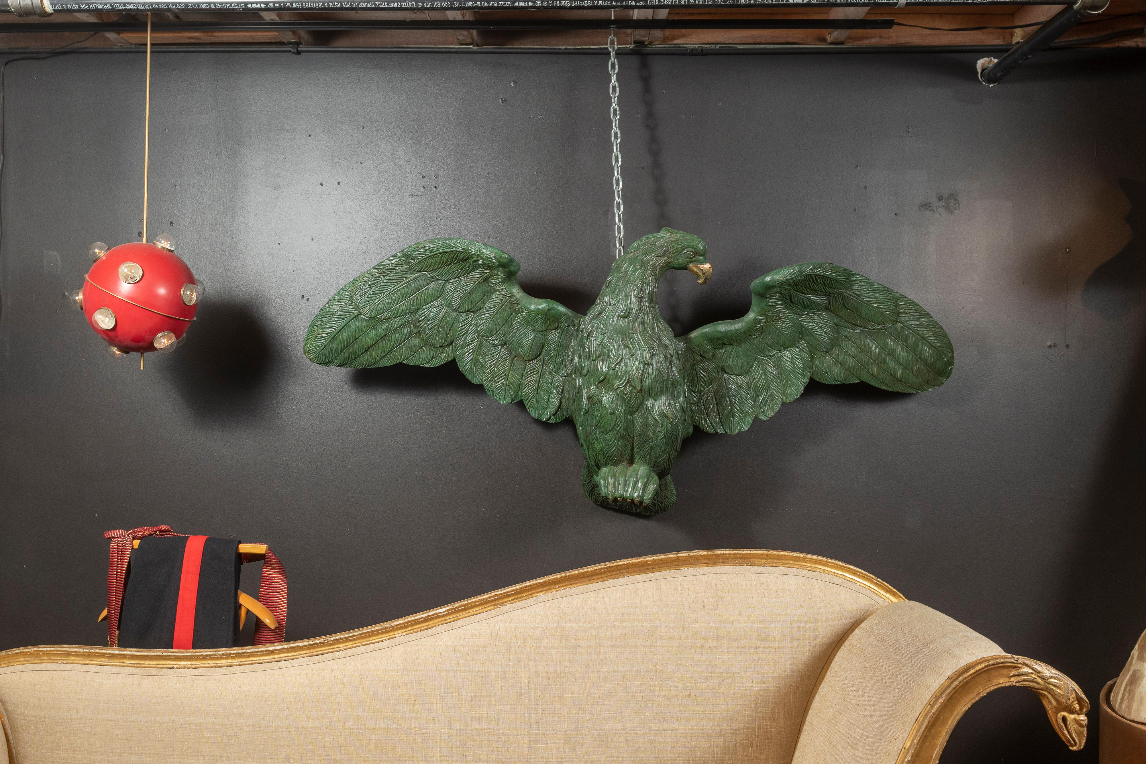 Antique carved wooden eagle painted green with gilded accents makes an impressive statement with its 69 inch wing span when hung in your home, office or business. The piece is in good condition considering its age and materials. The wings have been
