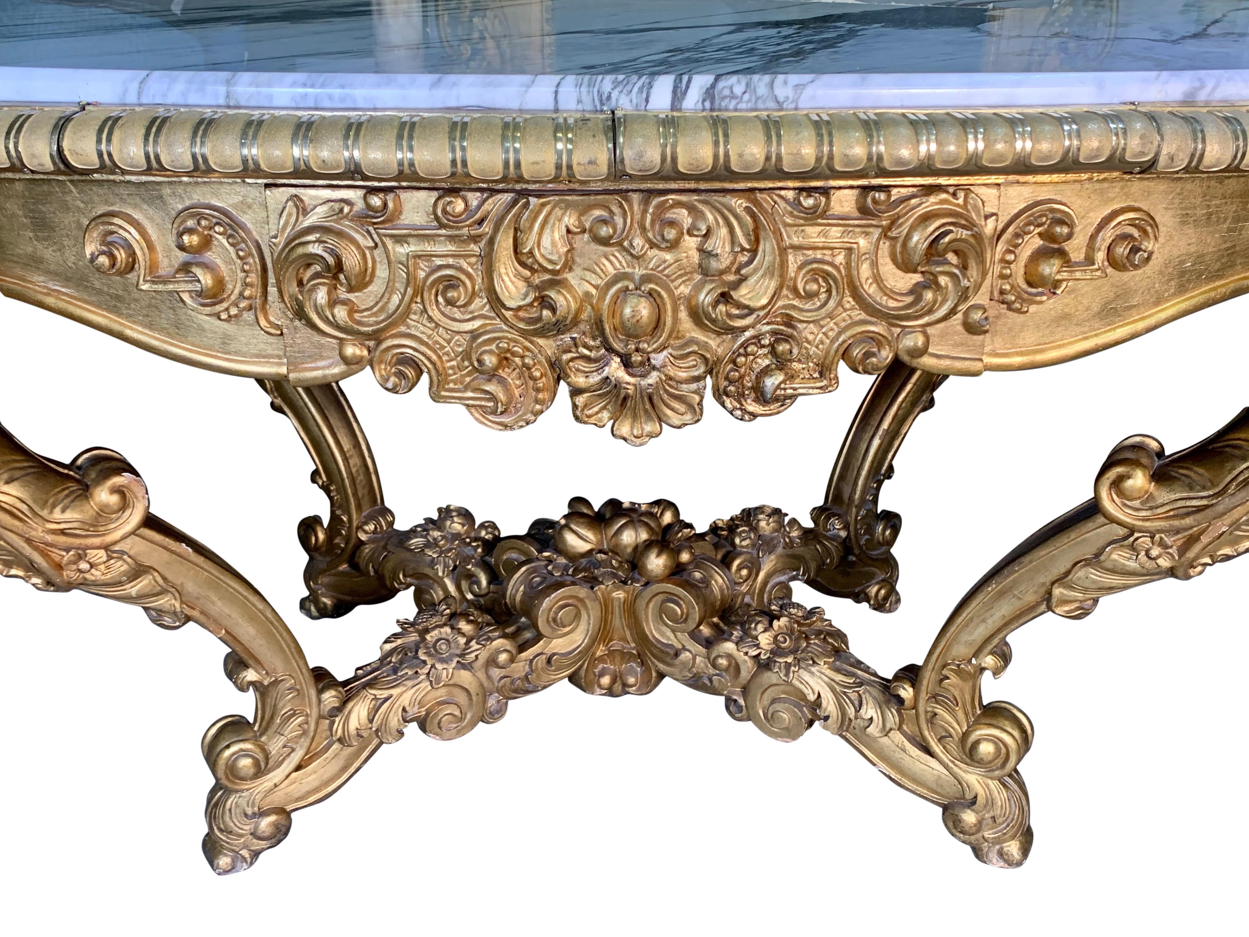 A stunning 19th century continental Rococo style oval hand carved giltwood and marble top center table with a single drawer. This large table is raised on four elegant cabriole legs joined by a stretcher with carved leaves flowers and fruits. The