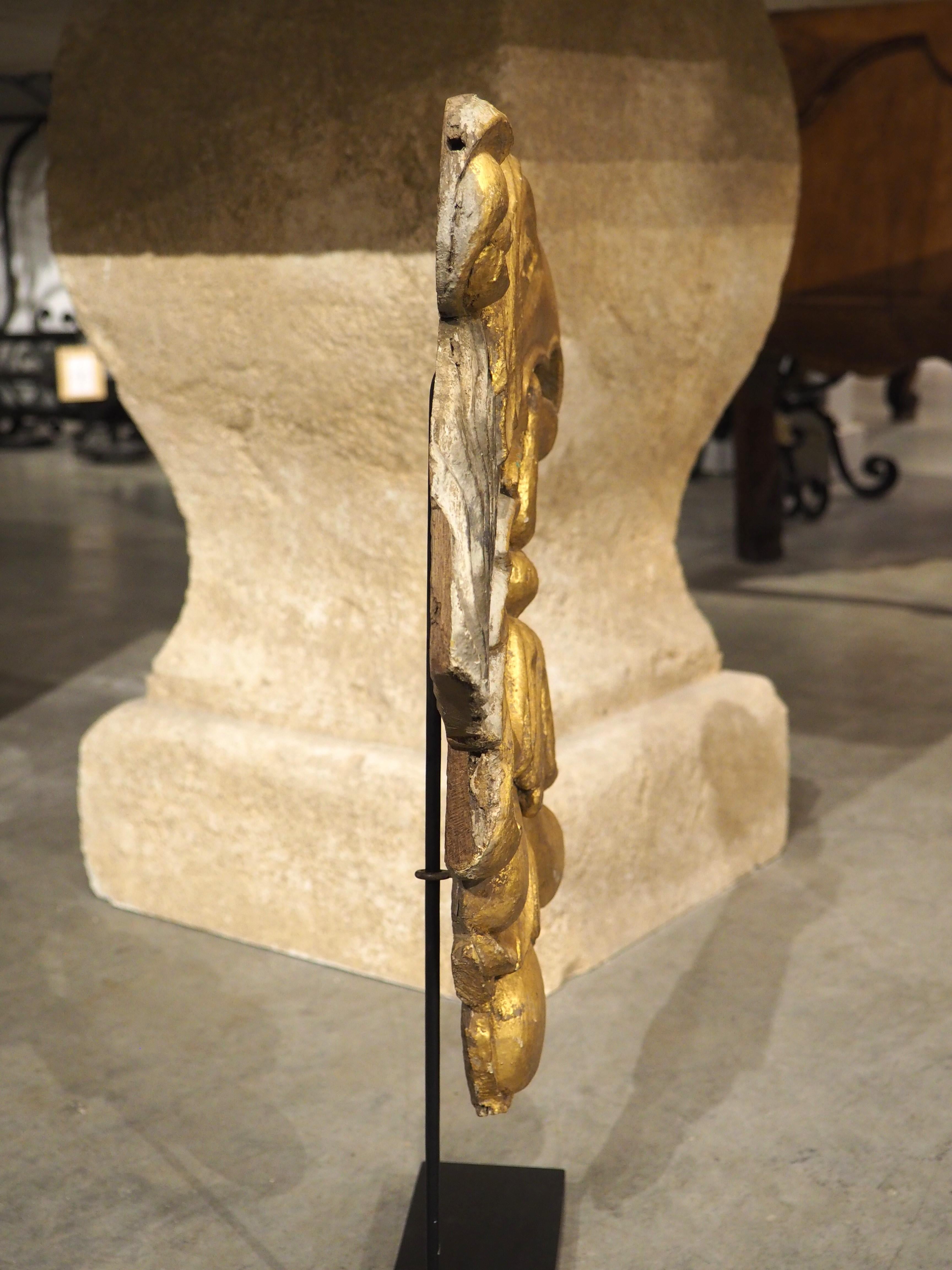 Sculptée à la main en Italie, vers 1750, cette grande tête d'aigle en bois doré sculpté a été montée plus récemment sur un socle peint en noir avec un fin bras en métal. L'oiseau a un grand margent feuillu accroché à son bec et une fleur en forme de